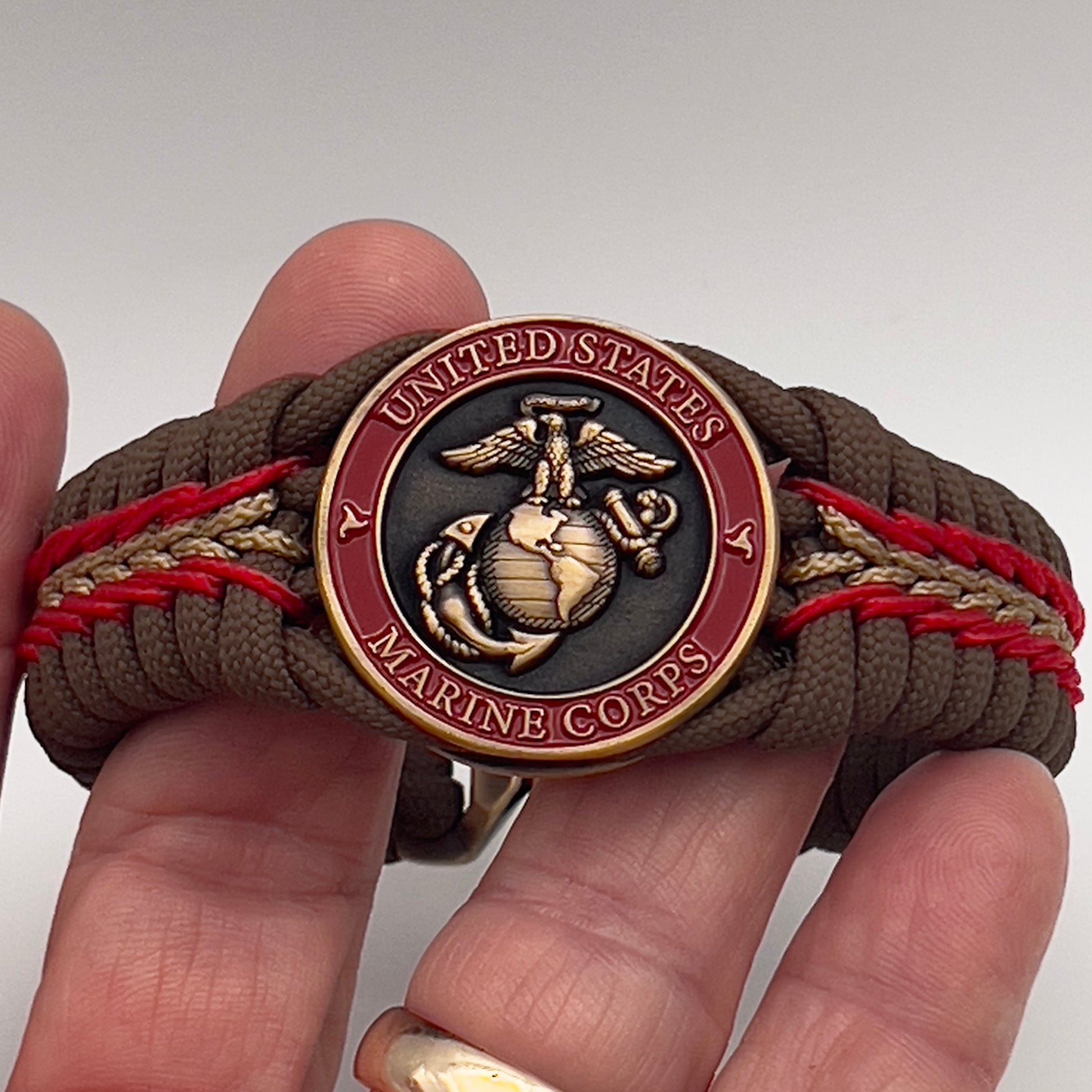 Thick, medium width, rigid and comfortable braided United States Marine Corps bracelet featuring a 24K antique gold plated USMC Eagle Globe and Anchor medallion, a gold Cobra style tactical buckle and woven with Coyote Brown 550 paracord and Imperial Red and Gold micro cord.
