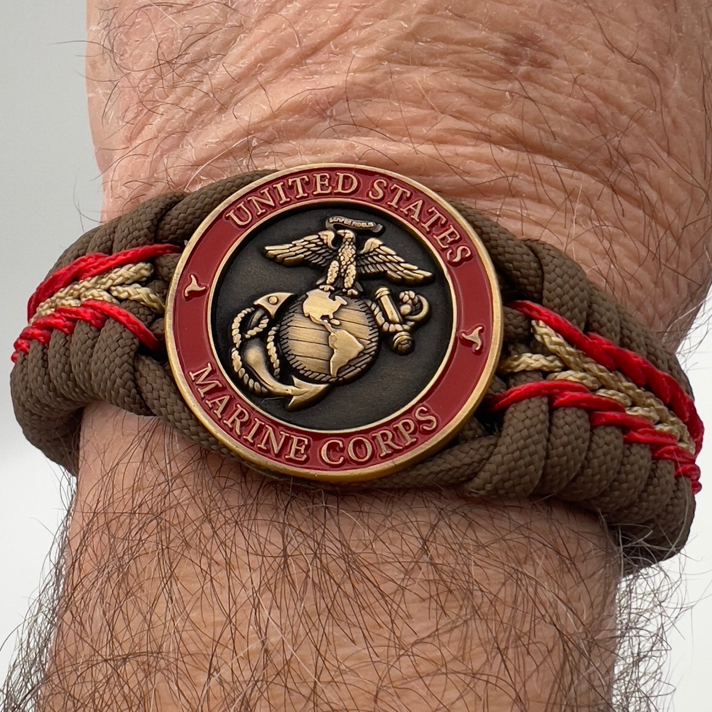 Thick, medium width, rigid and comfortable braided United States Marine Corps bracelet featuring a 24K antique gold plated USMC Eagle Globe and Anchor medallion, a gold Cobra style tactical buckle and woven with Coyote Brown 550 paracord and Imperial Red and Gold micro cord.