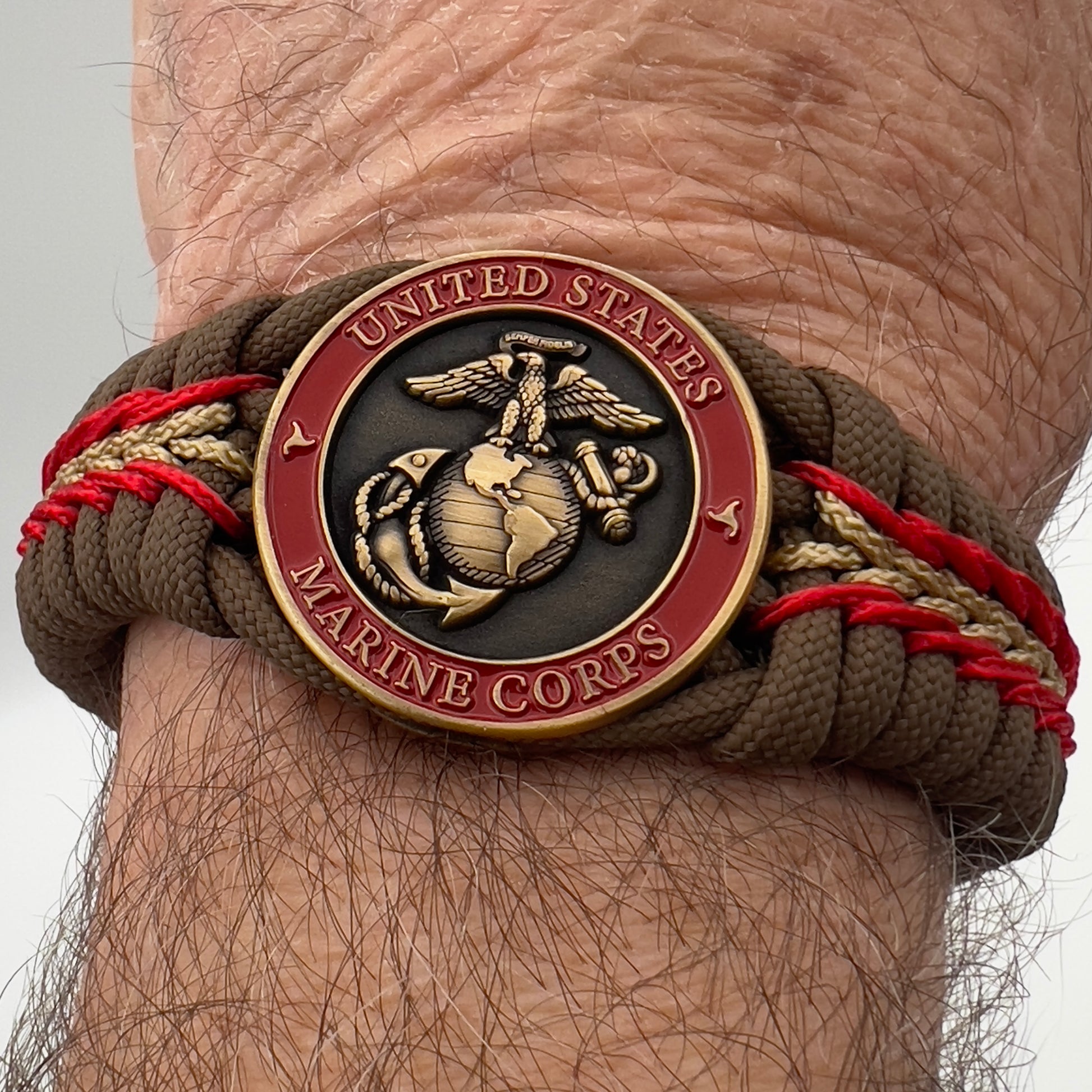 Thick, medium width, rigid and comfortable braided United States Marine Corps bracelet featuring a 24K antique gold plated USMC Eagle Globe and Anchor medallion, a gold Cobra style tactical buckle and woven with Coyote Brown 550 paracord and Imperial Red and Gold micro cord.
