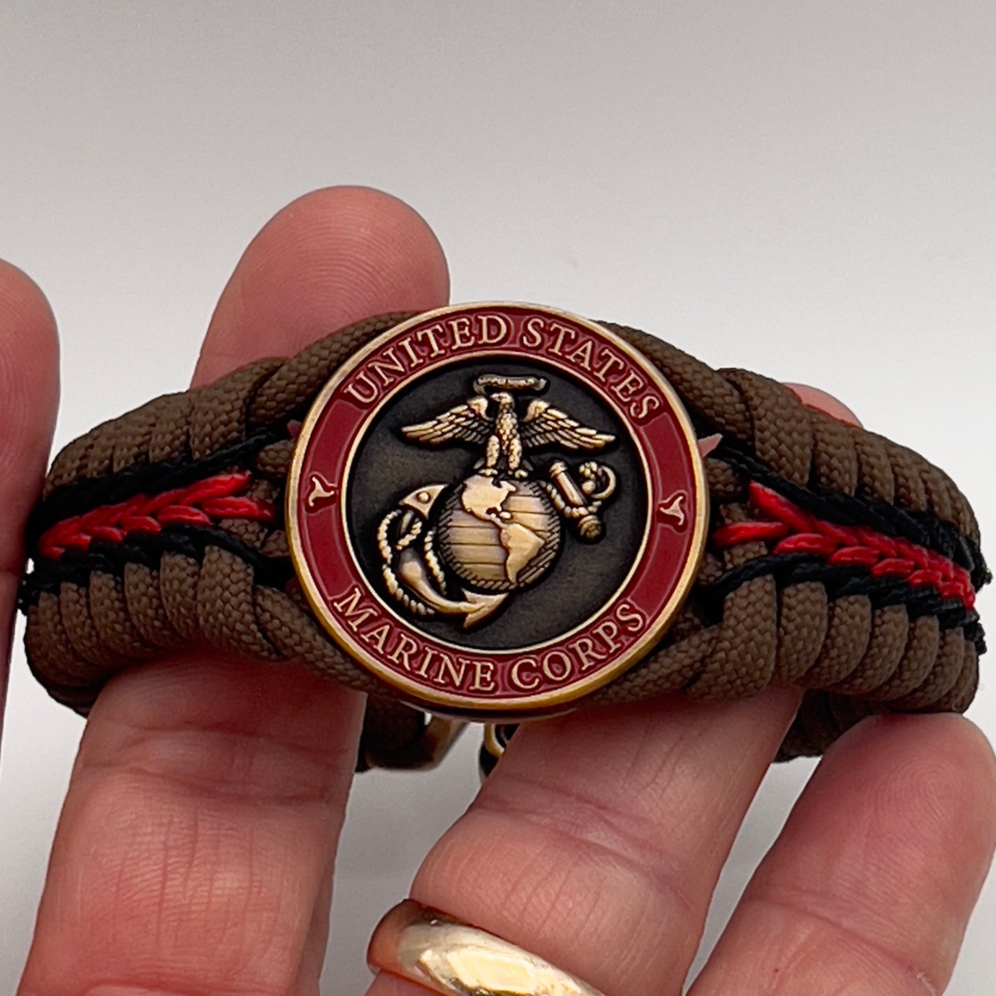 Thick, medium width, rigid and comfortable braided United States Marine Corps bracelet featuring a 24K antique gold plated USMC Eagle Globe and Anchor medallion, a gold Cobra style tactical buckle and woven with Coyote Brown 550 paracord and Imperial Red and Black micro cord.