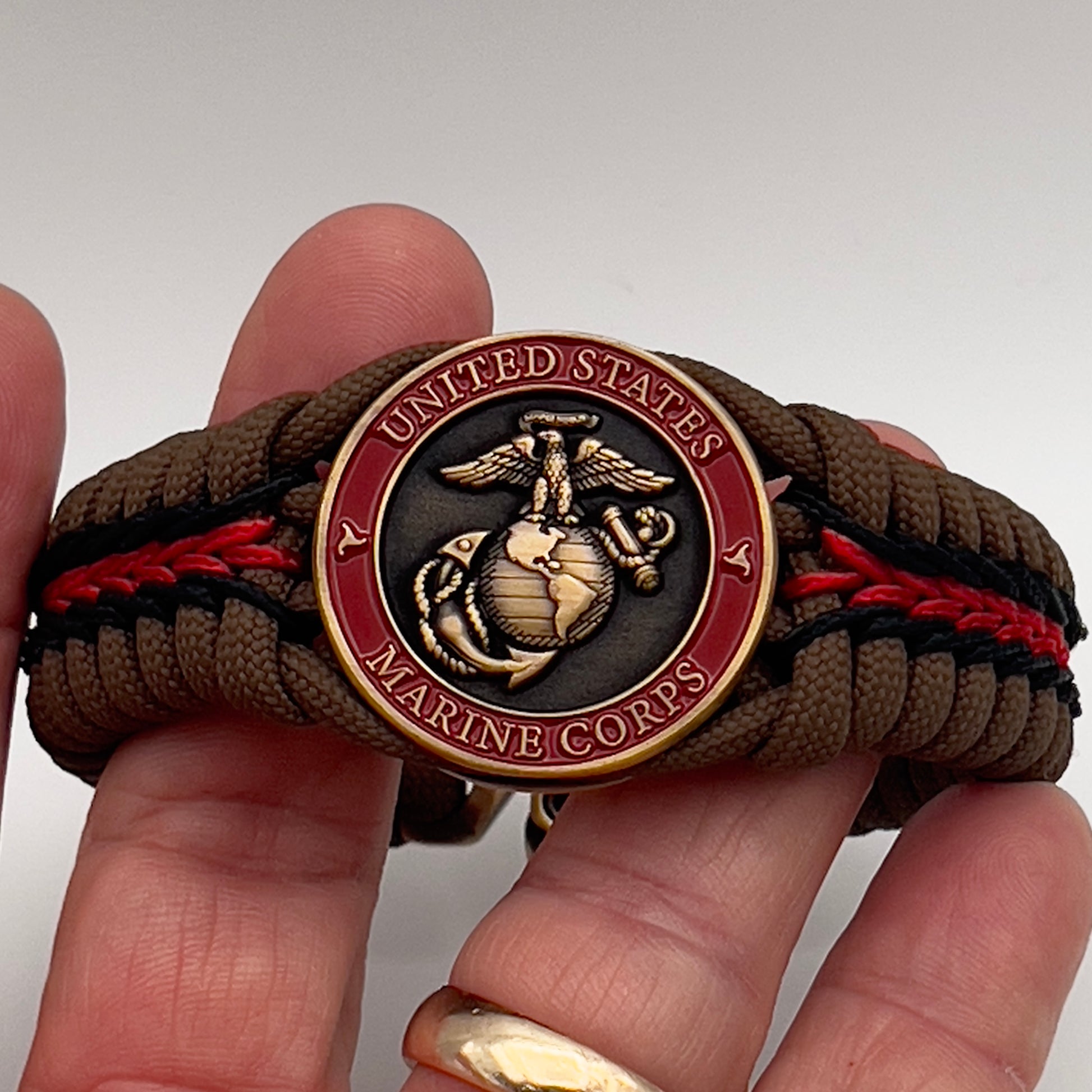 Thick, medium width, rigid and comfortable braided United States Marine Corps bracelet featuring a 24K antique gold plated USMC Eagle Globe and Anchor medallion, a gold Cobra style tactical buckle and woven with Coyote Brown 550 paracord and Imperial Red and Black micro cord.