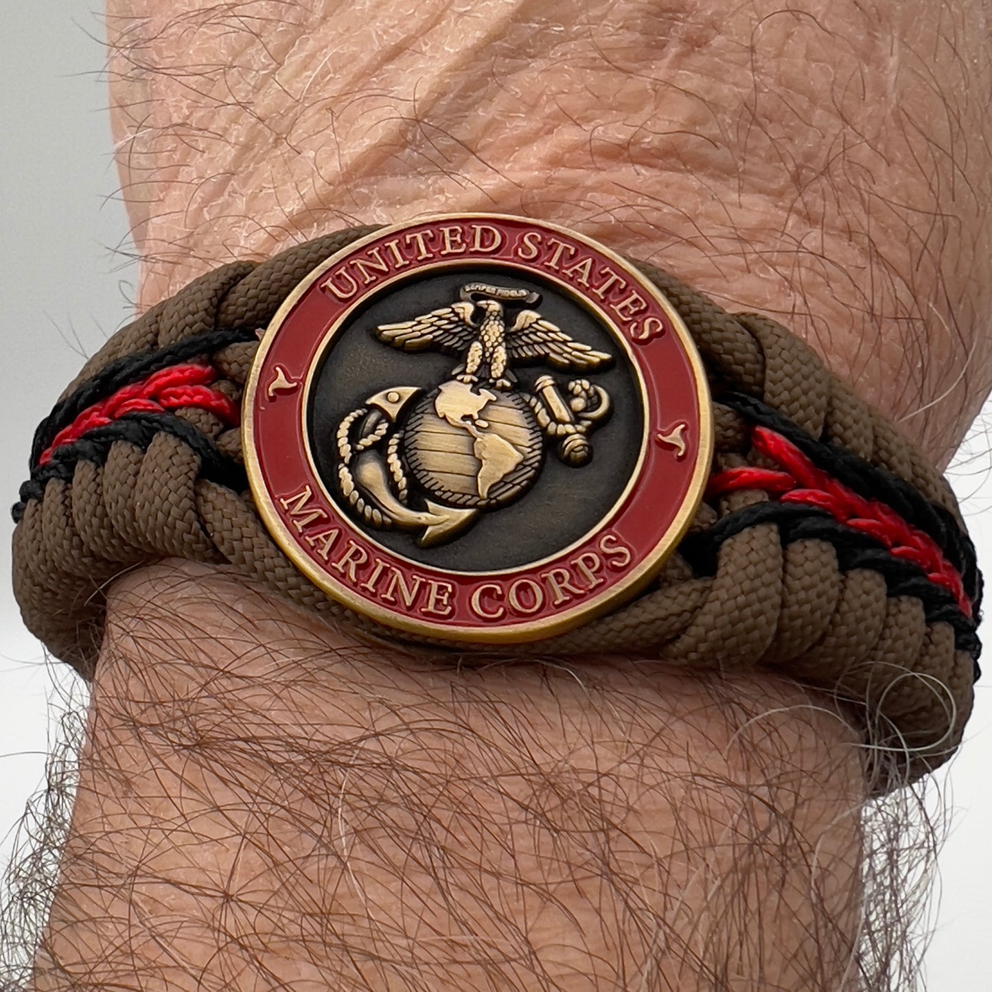 Thick, medium width, rigid and comfortable braided United States Marine Corps bracelet featuring a 24K antique gold plated USMC Eagle Globe and Anchor medallion, a gold Cobra style tactical buckle and woven with Coyote Brown 550 paracord and Imperial Red and Black micro cord.