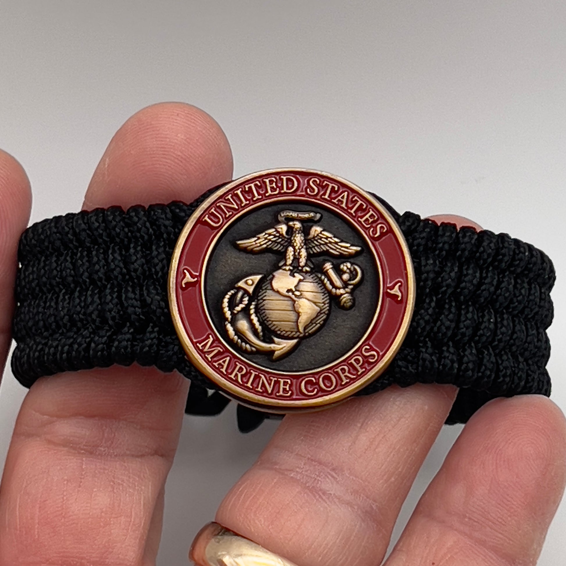 Thin, medium wide, very thin and flexible and comfortable braided United States Marine Corps bracelet featuring a 24K antique gold plated USMC Eagle Globe and Anchor medallion, a black Cobra style tactical buckle and woven with black Type-1 paracord.