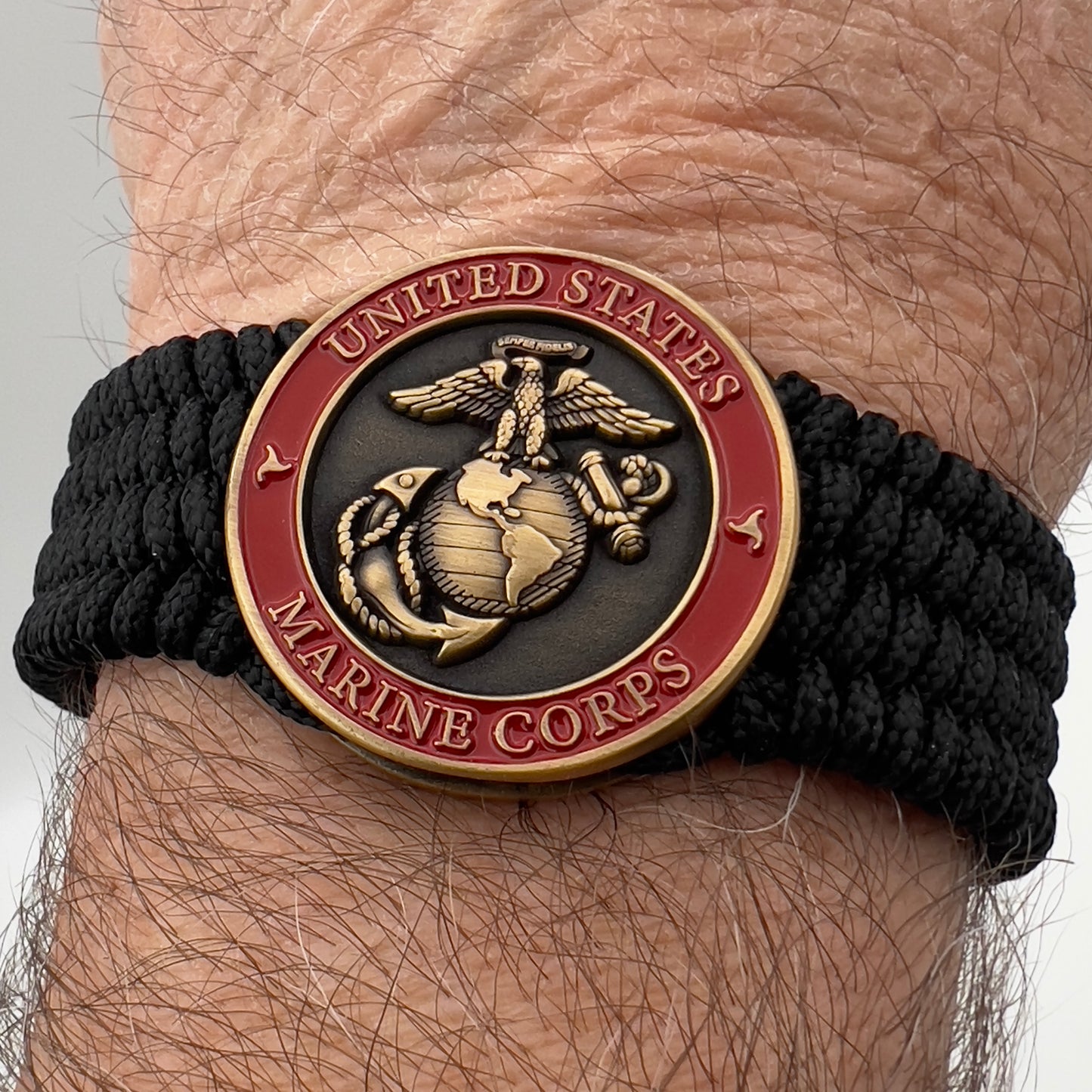 Thin, medium wide, very thin and flexible and comfortable braided United States Marine Corps bracelet featuring a 24K antique gold plated USMC Eagle Globe and Anchor medallion, a black Cobra style tactical buckle and woven with black Type-1 paracord.