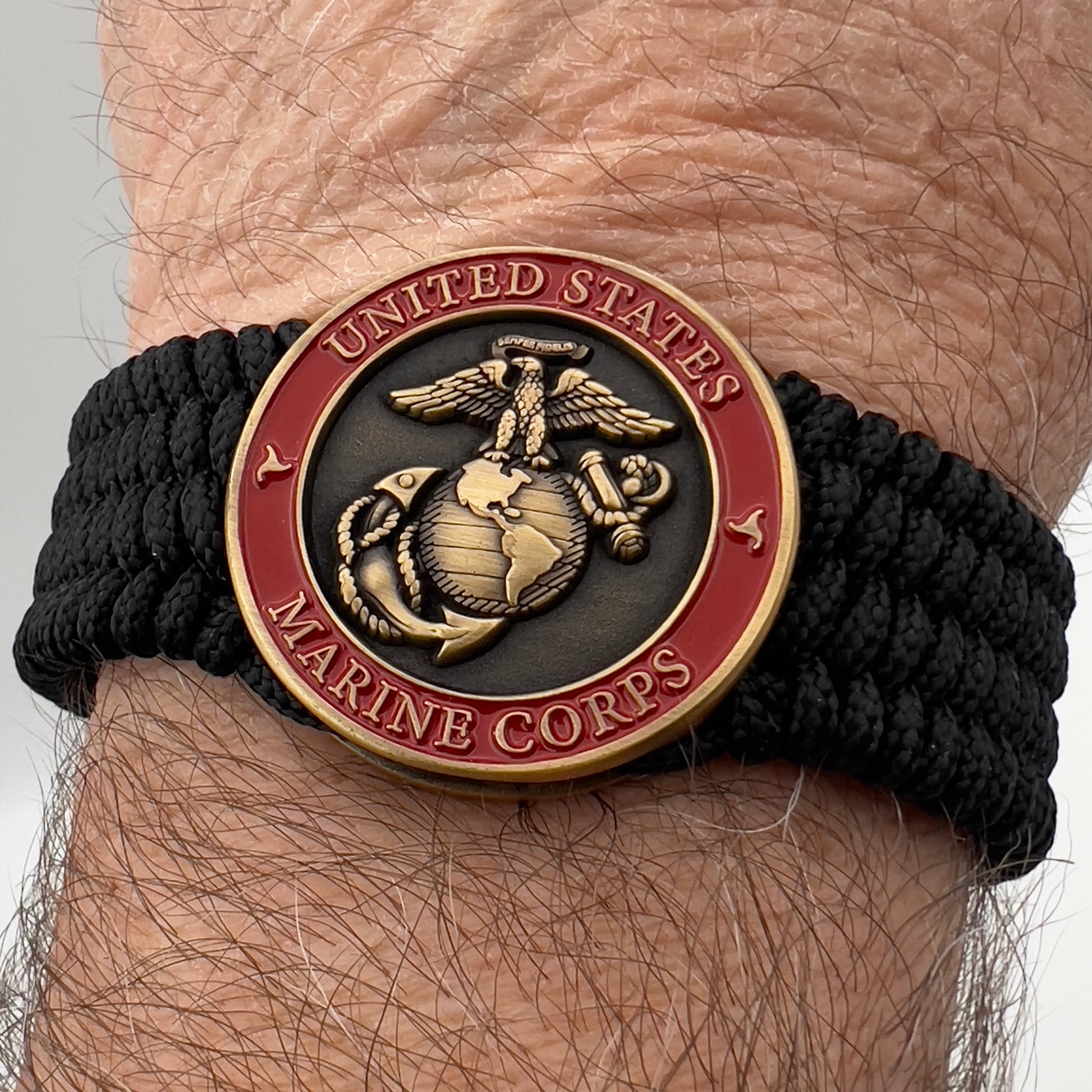 Thin, medium wide, very thin and flexible and comfortable braided United States Marine Corps bracelet featuring a 24K antique gold plated USMC Eagle Globe and Anchor medallion, a black Cobra style tactical buckle and woven with black Type-1 paracord.