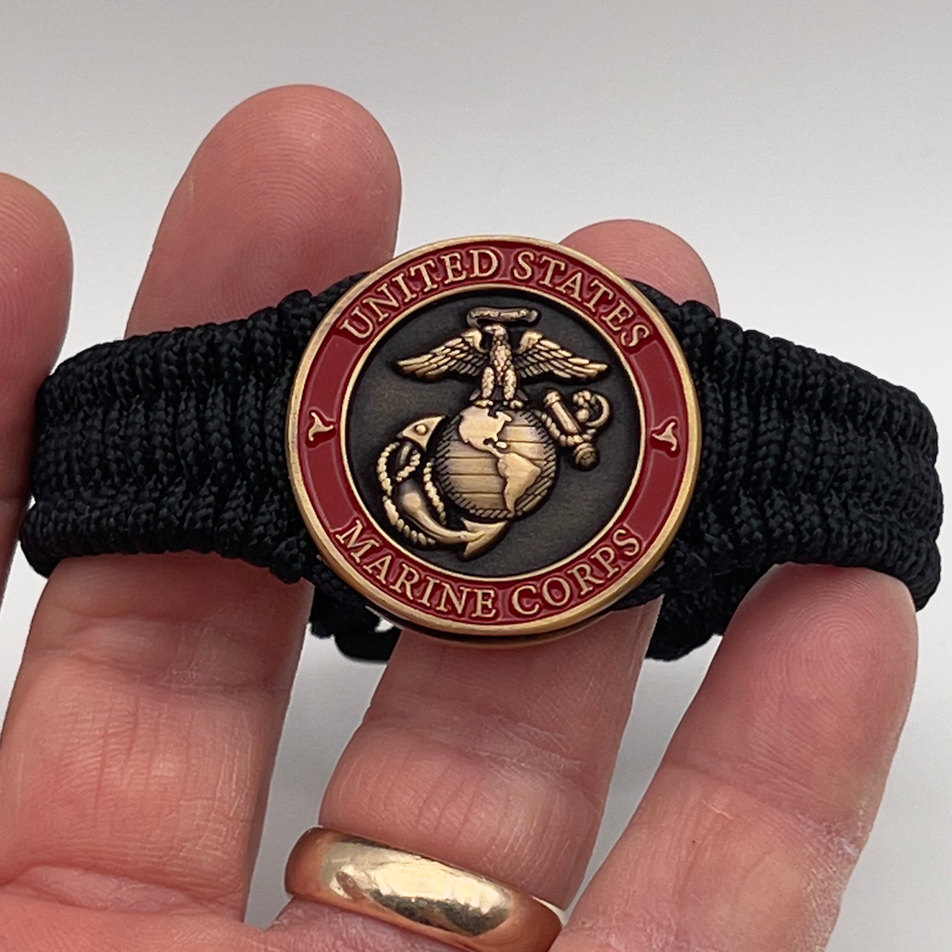 Thin, narrow, flexible and comfortable braided United States Marine Corps bracelet featuring a 24K antique gold plated USMC Eagle Globe and Anchor medallion, a black Cobra style tactical buckle and woven with black Type-1 paracord.