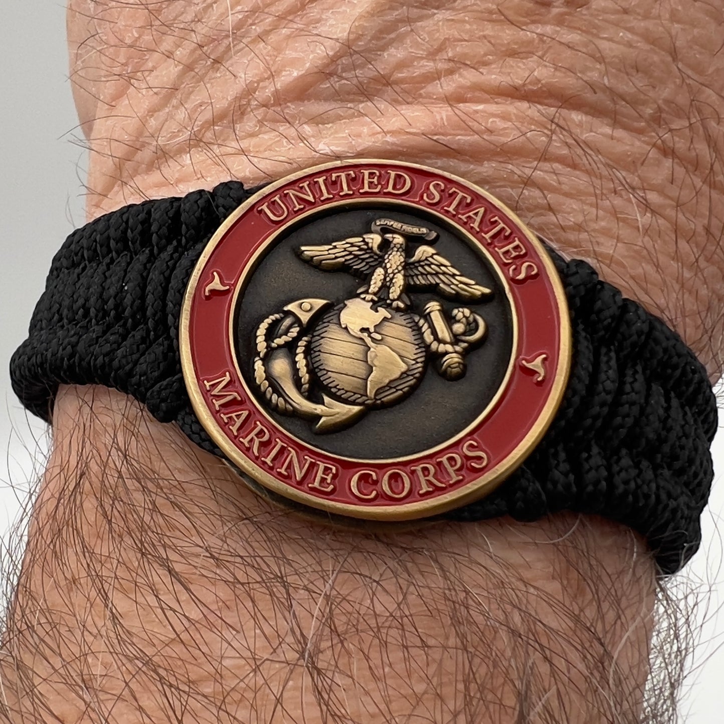 Thin, narrow, flexible and comfortable braided United States Marine Corps bracelet featuring a 24K antique gold plated USMC Eagle Globe and Anchor medallion, a black Cobra style tactical buckle and woven with black Type-1 paracord.