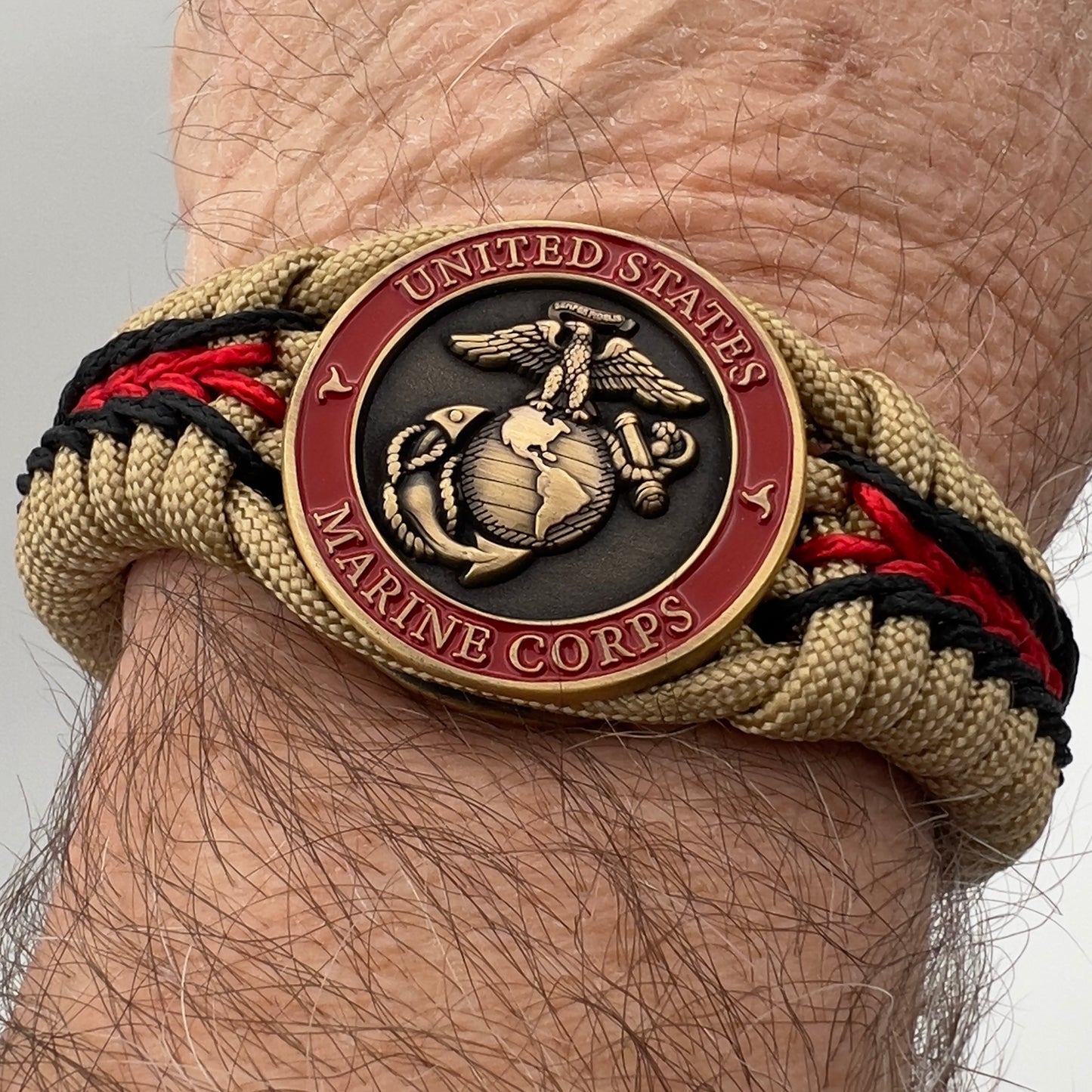 Thick, medium width, rigid and comfortable braided United States Marine Corps bracelet featuring a 24K antique gold plated USMC Eagle Globe and Anchor medallion, a gold Cobra style tactical buckle and woven with gold 550 paracord and Imperial red and black micro cord.