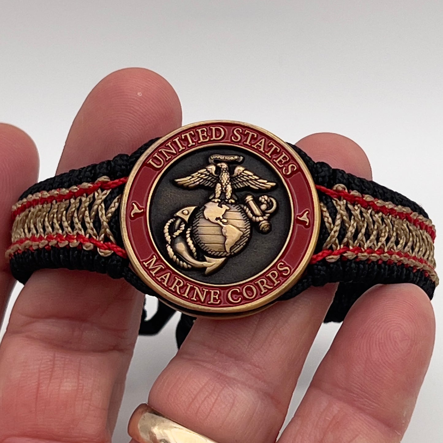 Thin, narrow, very thin and flexible and comfortable braided United States Marine Corps bracelet featuring a 24K antique gold plated USMC Eagle Globe and Anchor medallion, a black Cobra style tactical buckle and woven with black Type-1 paracord and Imperial Red and GOld nano cord.