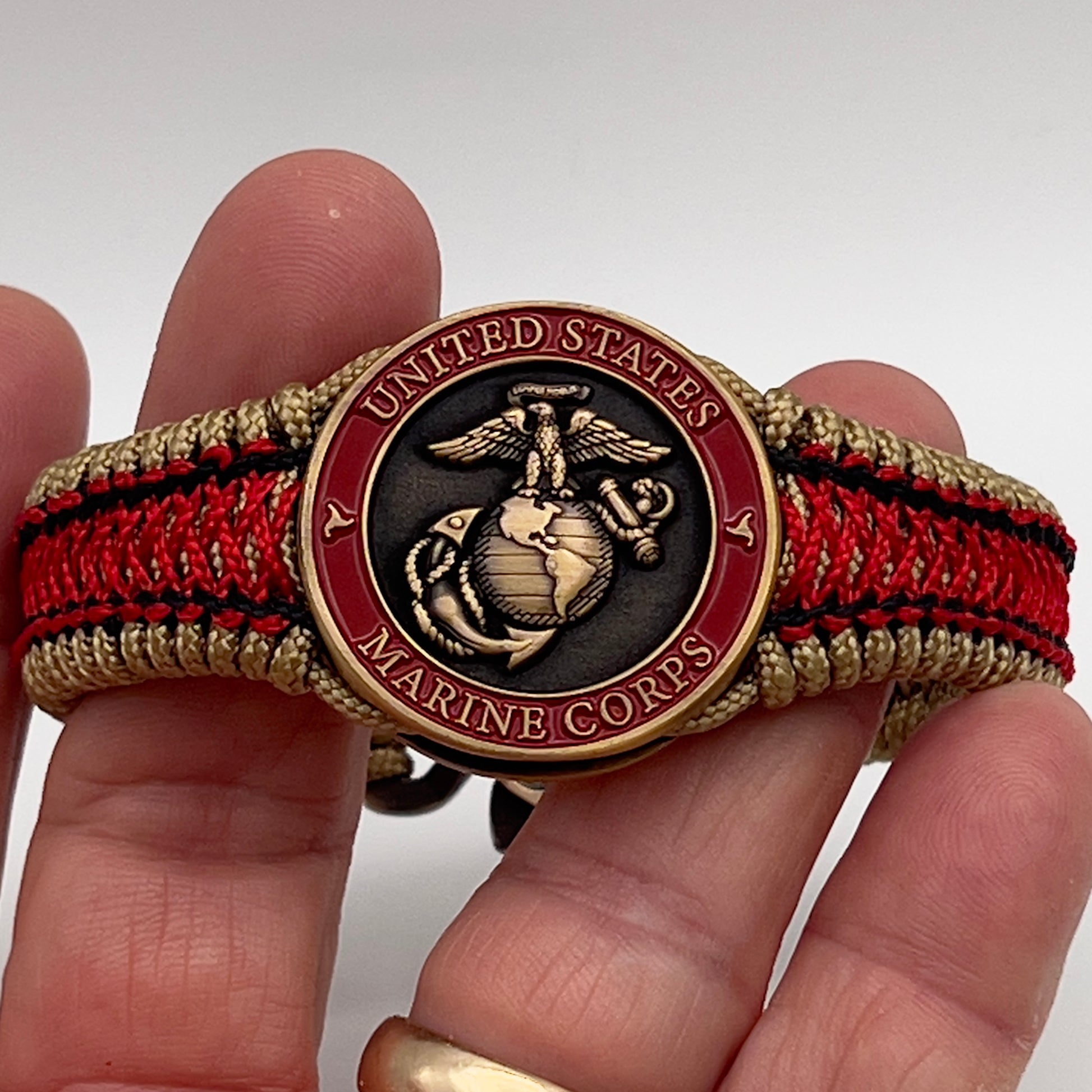 Thin, narrow, very thin and flexible and comfortable braided United States Marine Corps bracelet featuring a 24K antique gold plated USMC Eagle Globe and Anchor medallion, a gold Cobra style tactical buckle and woven with gold Type-1 paracord and Imperial Red and Black nano cord.