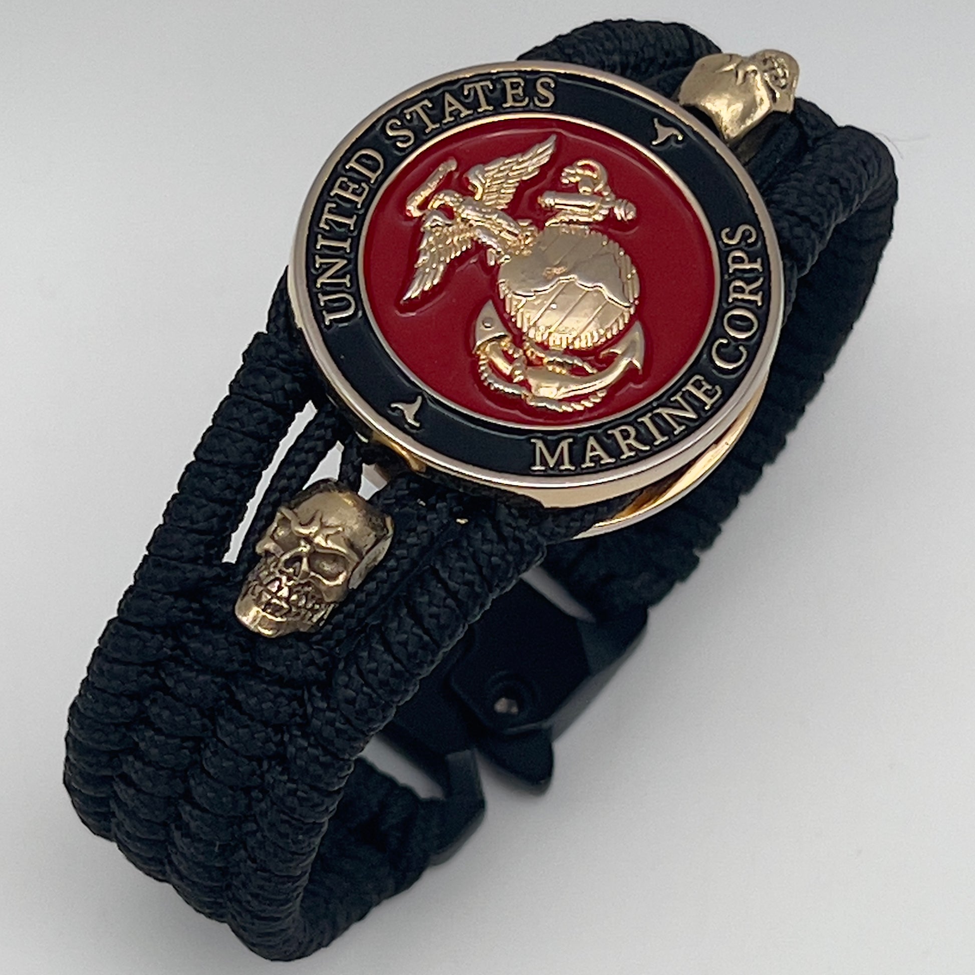 Thin, medium width, flexible and comfortable braided United States Marine Corps bracelet featuring a 24K gold plated USMC officer Eagle Globe and Anchor medallion, two gold plated skulls, a black Cobra style tactical buckle and woven with black Type-1 paracord.