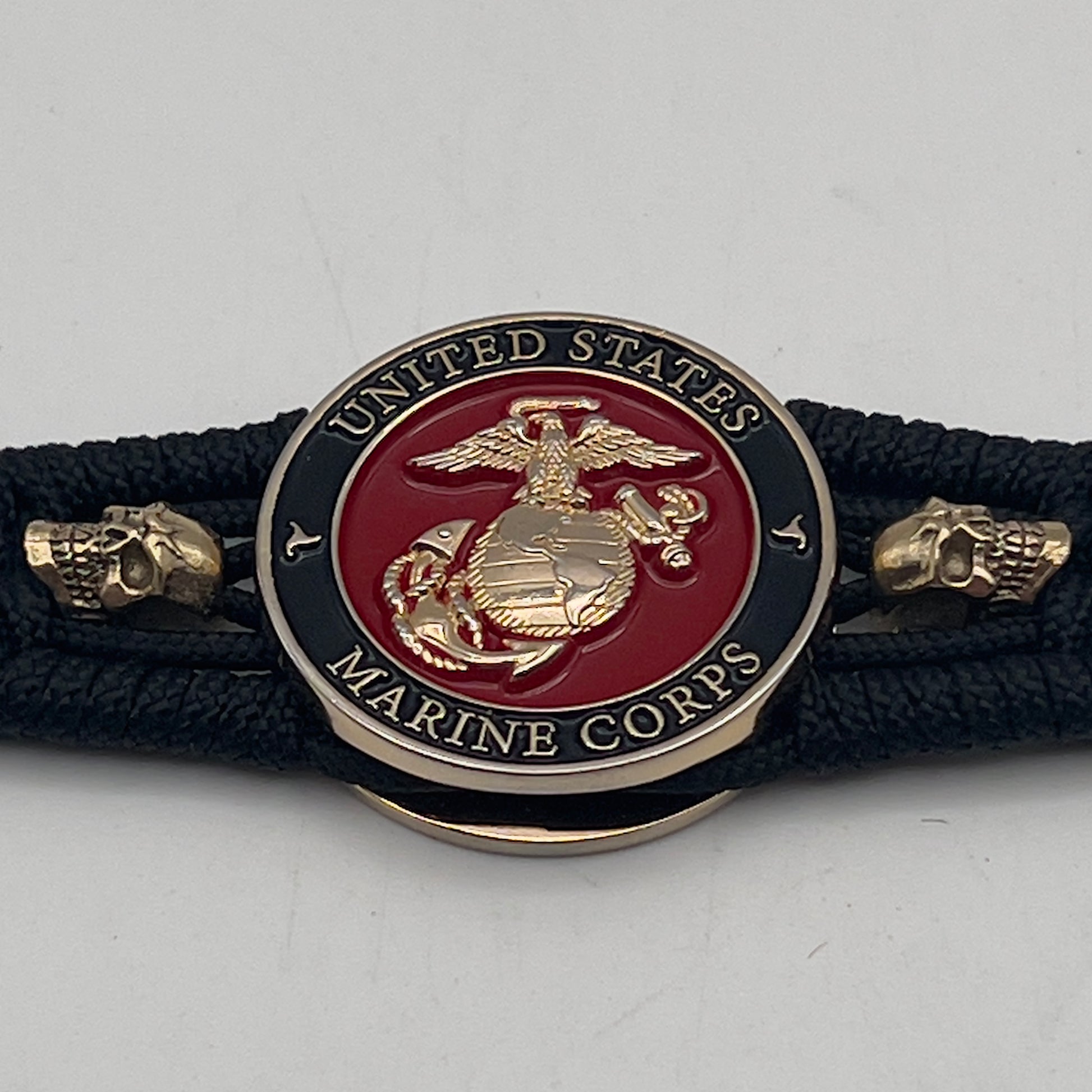 Thin, medium width, flexible and comfortable braided United States Marine Corps bracelet featuring a 24K gold plated USMC officer Eagle Globe and Anchor medallion, two gold plated skulls, a black Cobra style tactical buckle and woven with black Type-1 paracord.