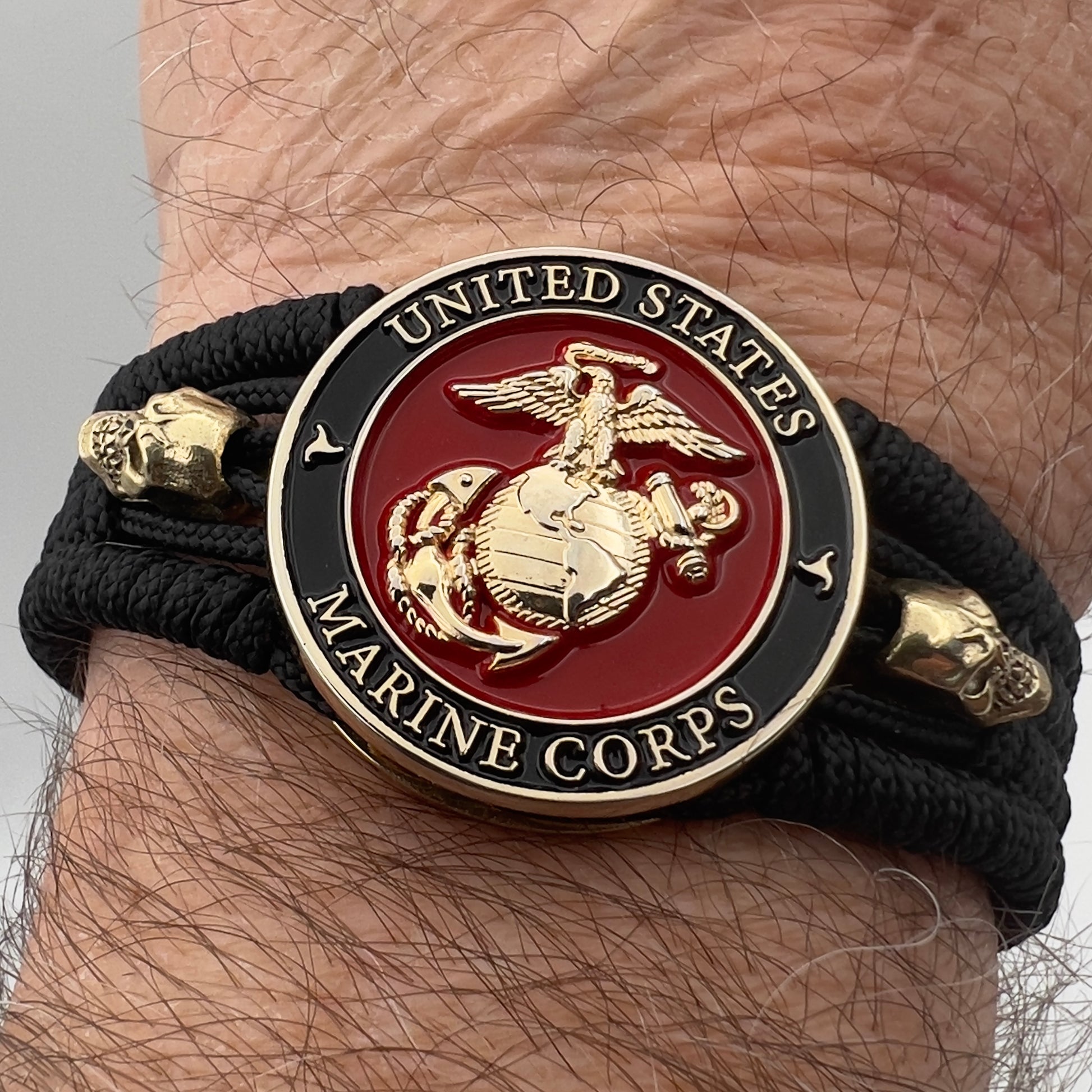 Thin, medium width, flexible and comfortable braided United States Marine Corps bracelet featuring a 24K gold plated USMC officer Eagle Globe and Anchor medallion, two gold plated skulls, a black Cobra style tactical buckle and woven with black Type-1 paracord.