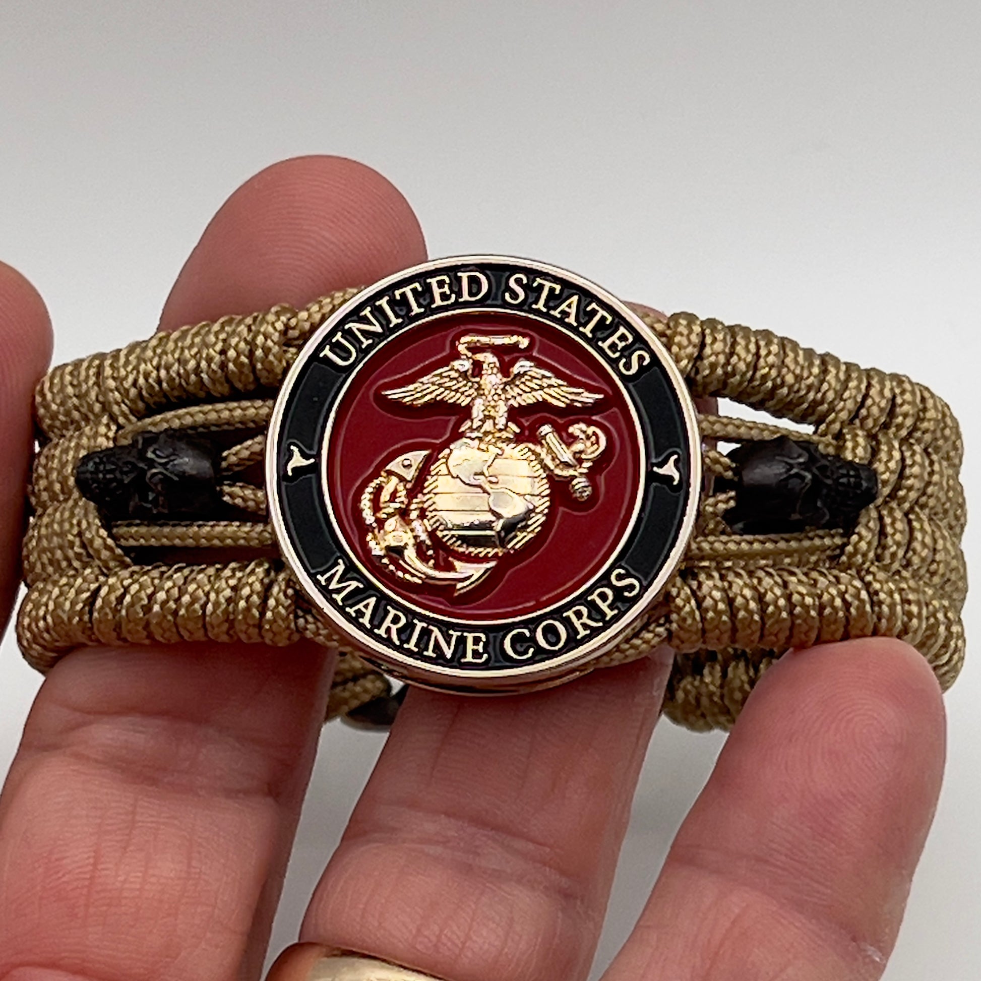 Thin, medium width, flexible and comfortable braided United States Marine Corps bracelet featuring a 24K gold plated USMC officer Eagle Globe and Anchor medallion, two black micro skulls, a gold Cobra style tactical buckle and woven with gold Type-1 paracord.