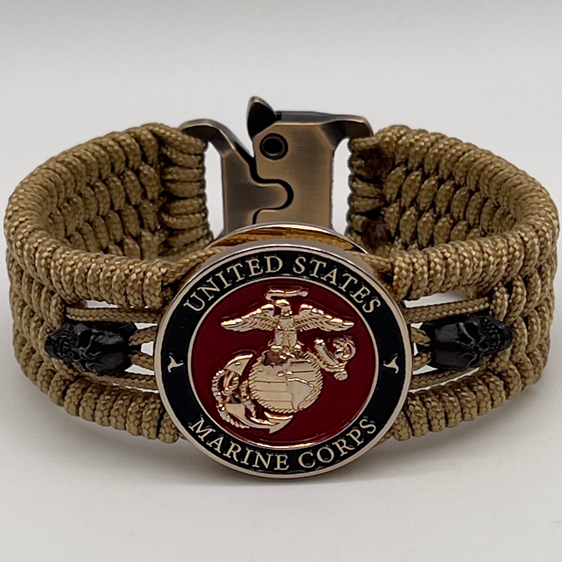 Thin, medium width, flexible and comfortable braided United States Marine Corps bracelet featuring a 24K gold plated USMC officer Eagle Globe and Anchor medallion, two black micro skulls, a gold Cobra style tactical buckle and woven with gold Type-1 paracord.