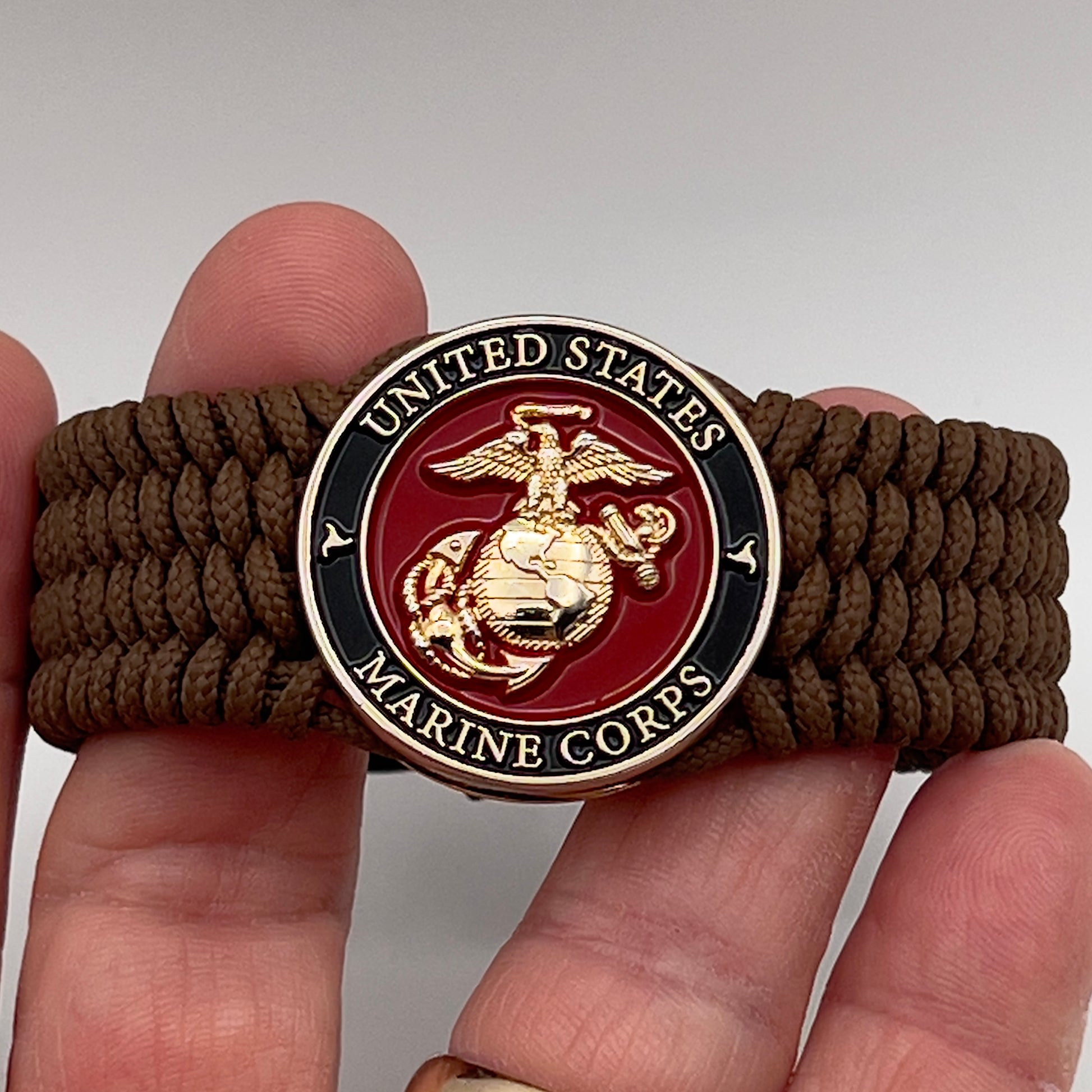 Thin, medium width, flexible and comfortable braided United States Marine Corps bracelet featuring a 24K gold plated USMC officer Eagle Globe and Anchor medallion, a gold Cobra style tactical buckle and woven with Coyote Brown Type-1 paracord.