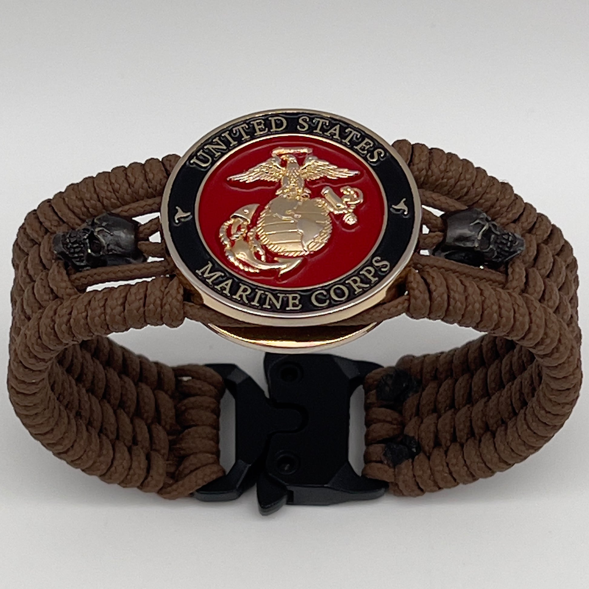 Thin, medium width, flexible and comfortable braided United States Marine Corps bracelet featuring a 24K gold plated USMC officer Eagle Globe and Anchor medallion, two black micro skulls, a black Cobra style tactical buckle and woven with Coyote Brown Type-1 paracord.