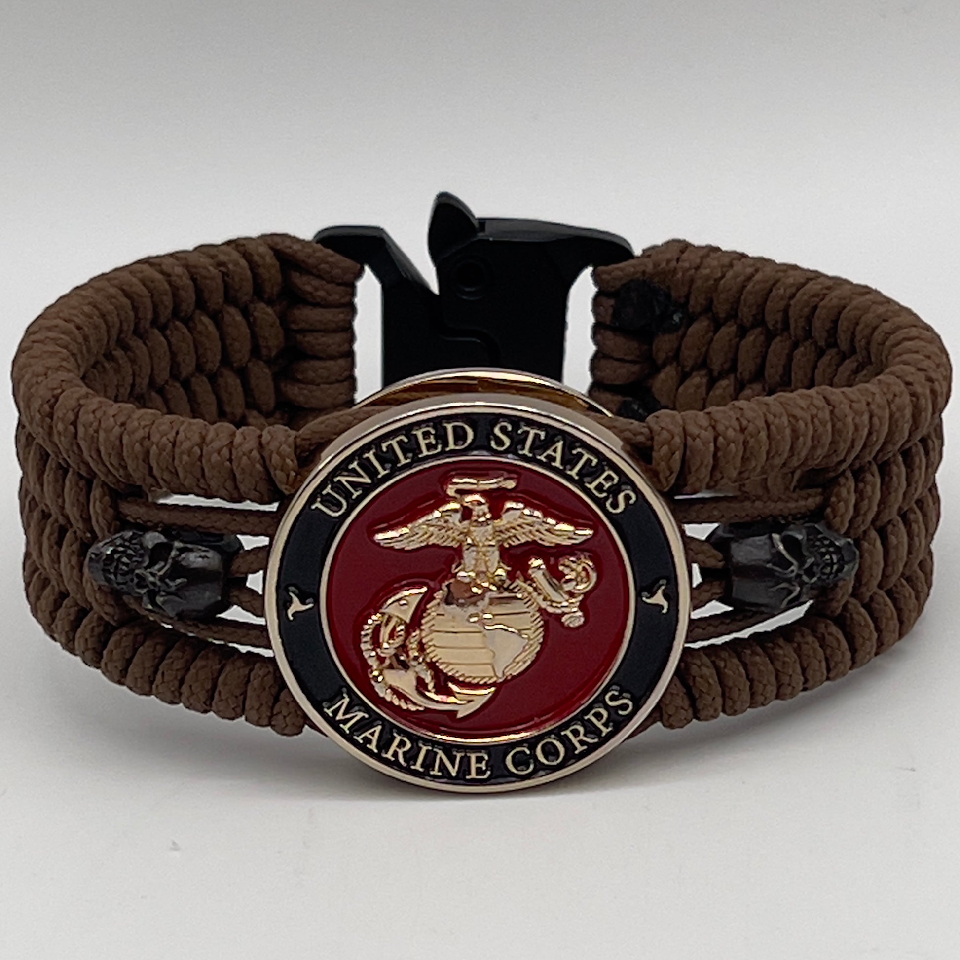 Thin, medium width, flexible and comfortable braided United States Marine Corps bracelet featuring a 24K gold plated USMC officer Eagle Globe and Anchor medallion, two black micro skulls, a black Cobra style tactical buckle and woven with Coyote Brown Type-1 paracord.