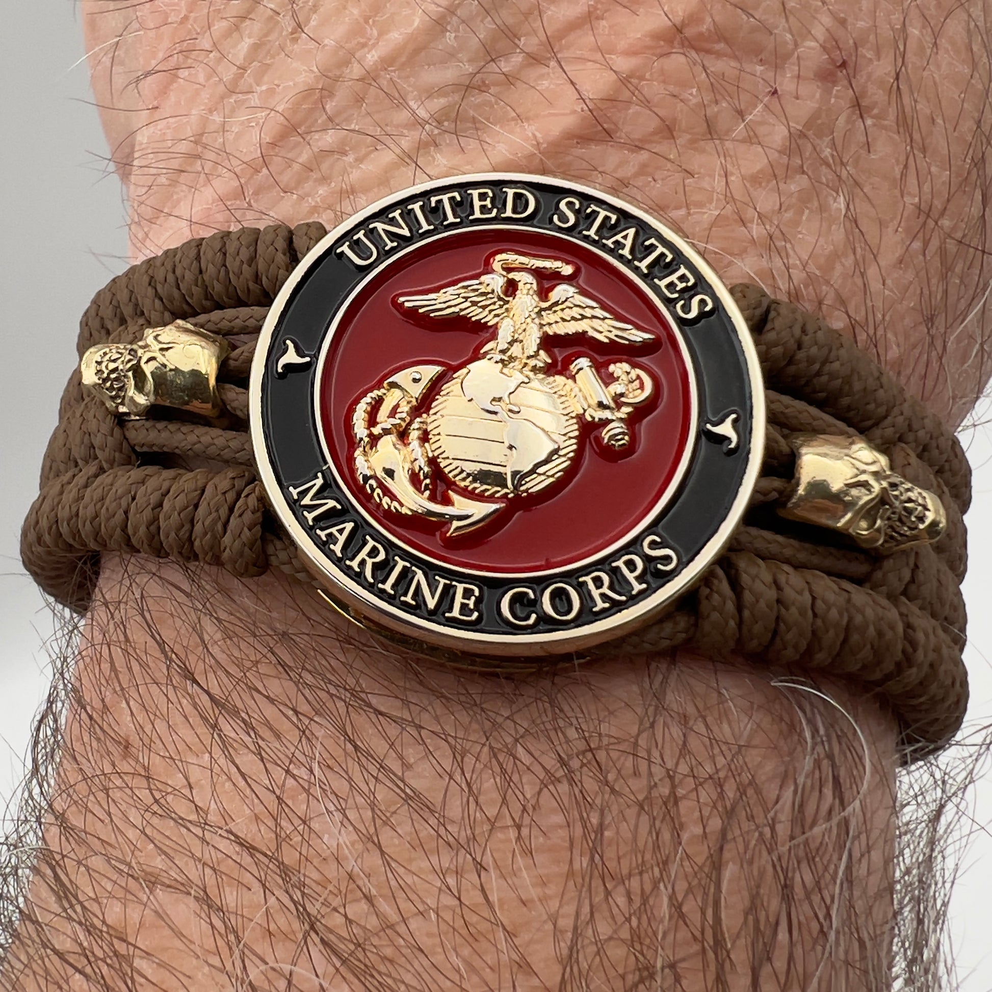 Thin, medium width, flexible and comfortable braided United States Marine Corps bracelet featuring a 24K gold plated USMC officer Eagle Globe and Anchor medallion, two gold plated skulls, a gold Cobra style tactical buckle and woven with Coyote Brown Type-1 paracord.