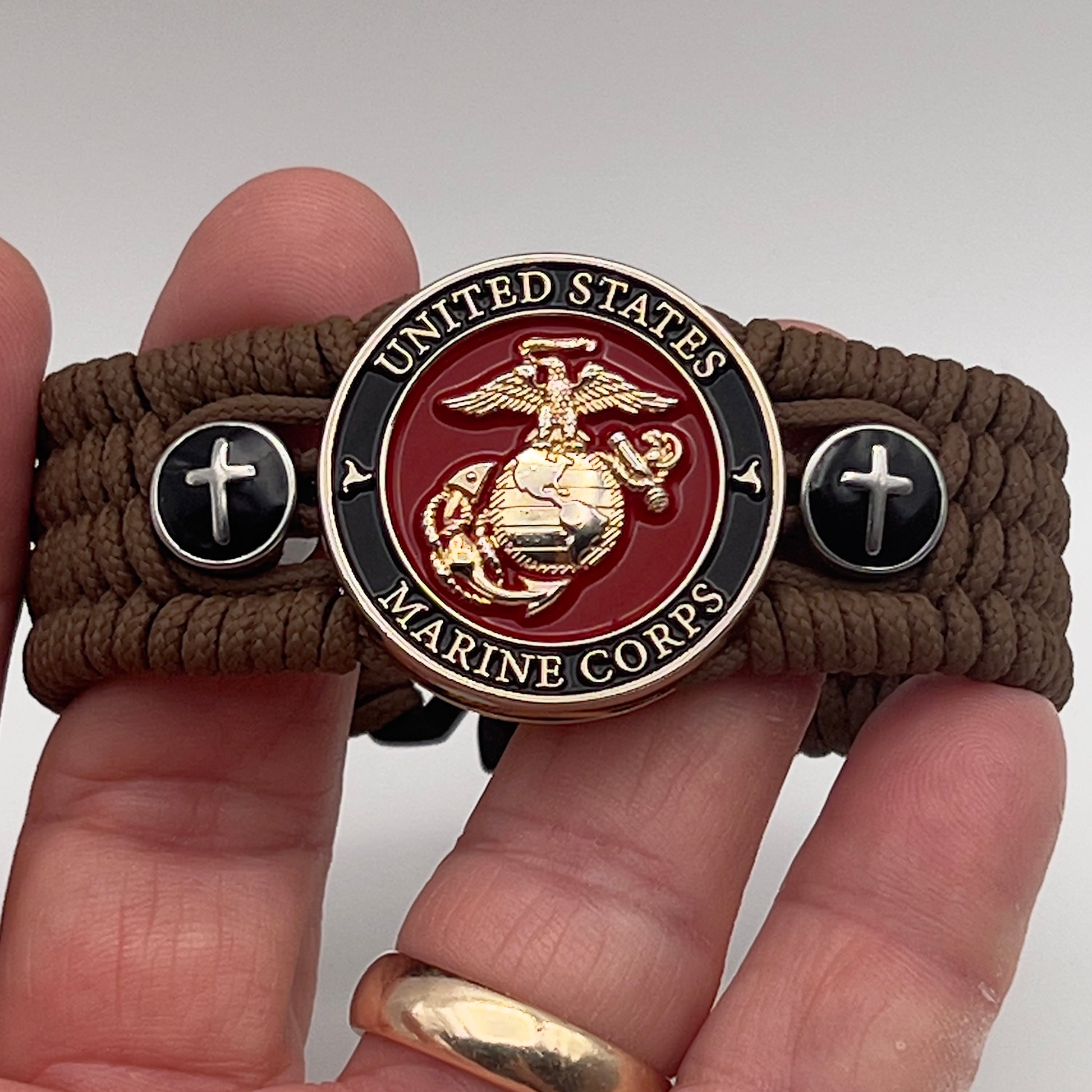 Thin, medium width, flexible and comfortable braided United States Marine Corps bracelet featuring a 24K gold plated USMC officer Eagle Globe and Anchor medallion, two Christian crosses, a black Cobra style tactical buckle and woven with Coyote Brown Type-1 paracord.