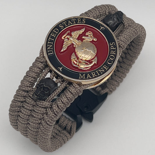 Thin, medium width, flexible and comfortable braided United States Marine Corps bracelet featuring a 24K gold plated USMC officer Eagle Globe and Anchor medallion, two black skulls, a black Cobra style tactical buckle and woven with tan Type-1 paracord.