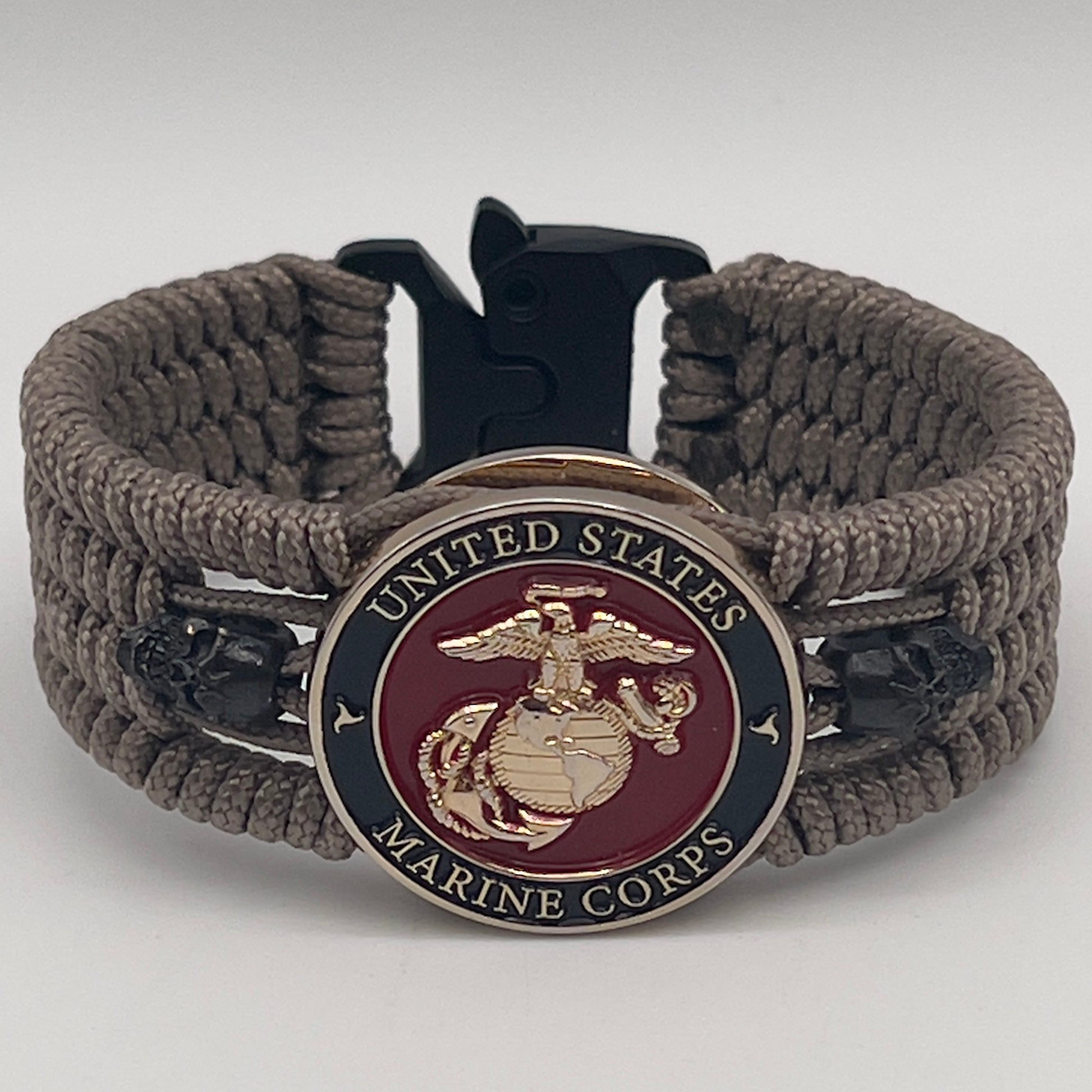 Thin, medium width, flexible and comfortable braided United States Marine Corps bracelet featuring a 24K gold plated USMC officer Eagle Globe and Anchor medallion, two black skulls, a black Cobra style tactical buckle and woven with tan Type-1 paracord.