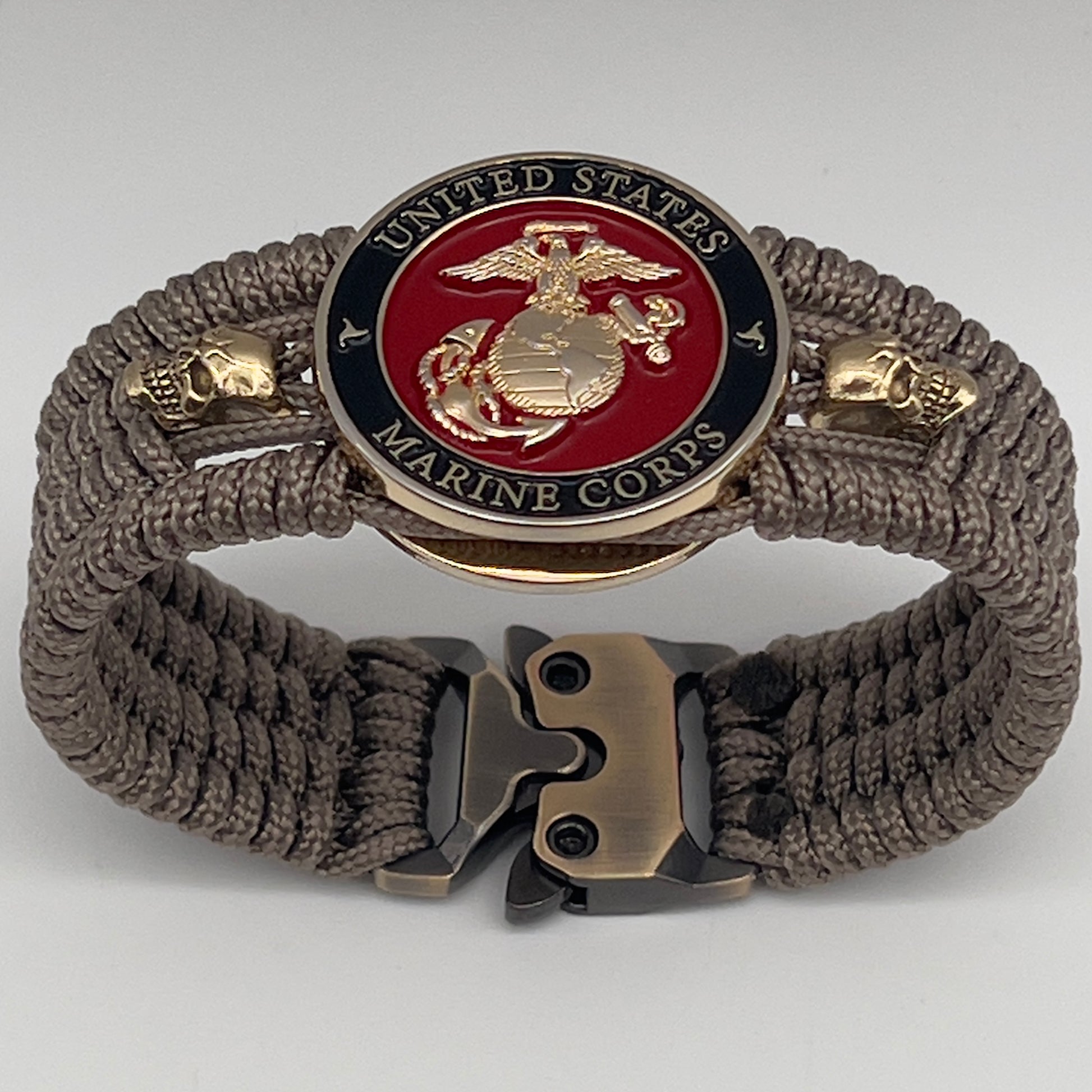 Thin, medium width, flexible and comfortable braided United States Marine Corps bracelet featuring a 24K gold plated USMC officer Eagle Globe and Anchor medallion, two gold plated skulls, a gold Cobra style tactical buckle and woven with Tan Type-1 paracord.