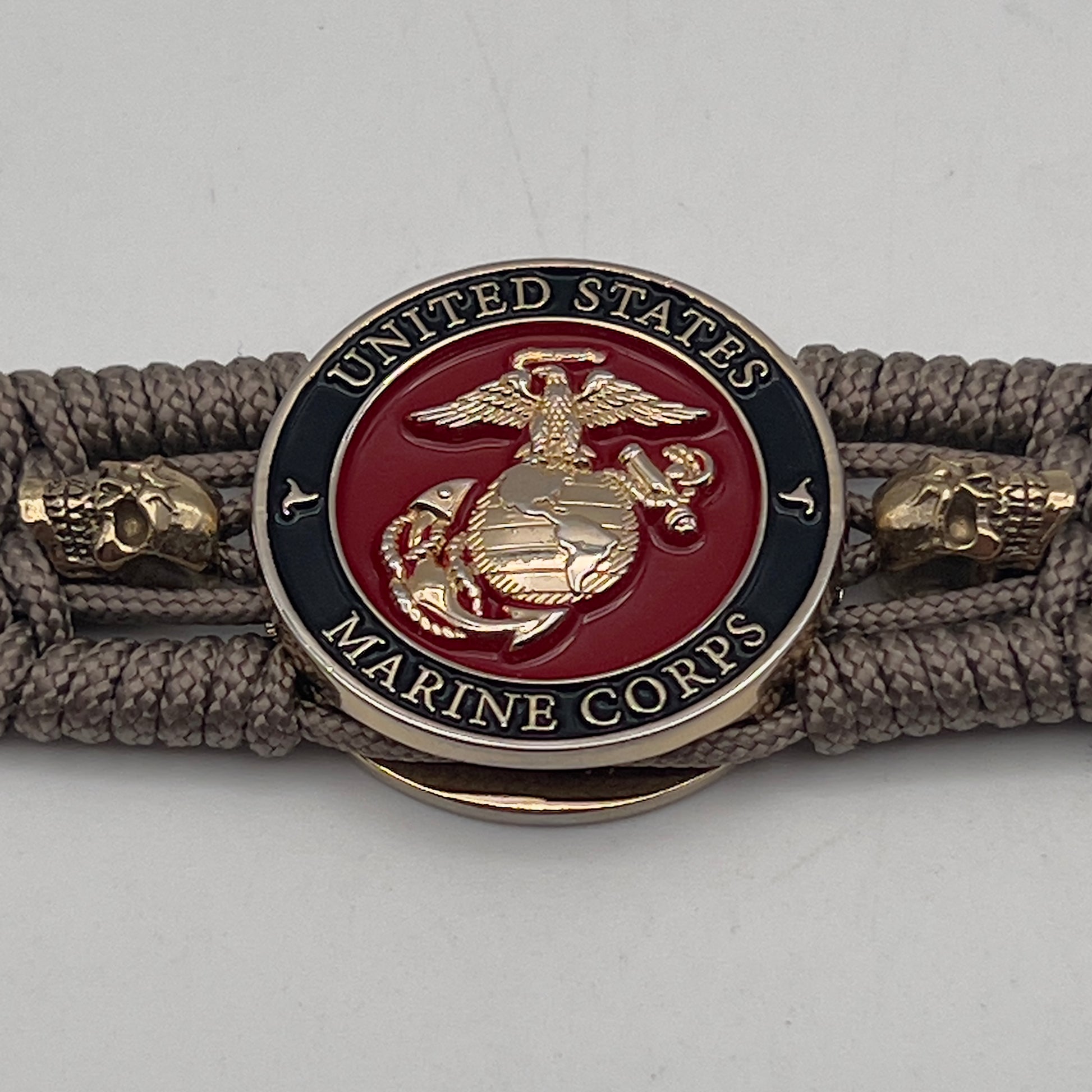 Thin, medium width, flexible and comfortable braided United States Marine Corps bracelet featuring a 24K gold plated USMC officer Eagle Globe and Anchor medallion, two gold plated skulls, a gold Cobra style tactical buckle and woven with Tan Type-1 paracord.