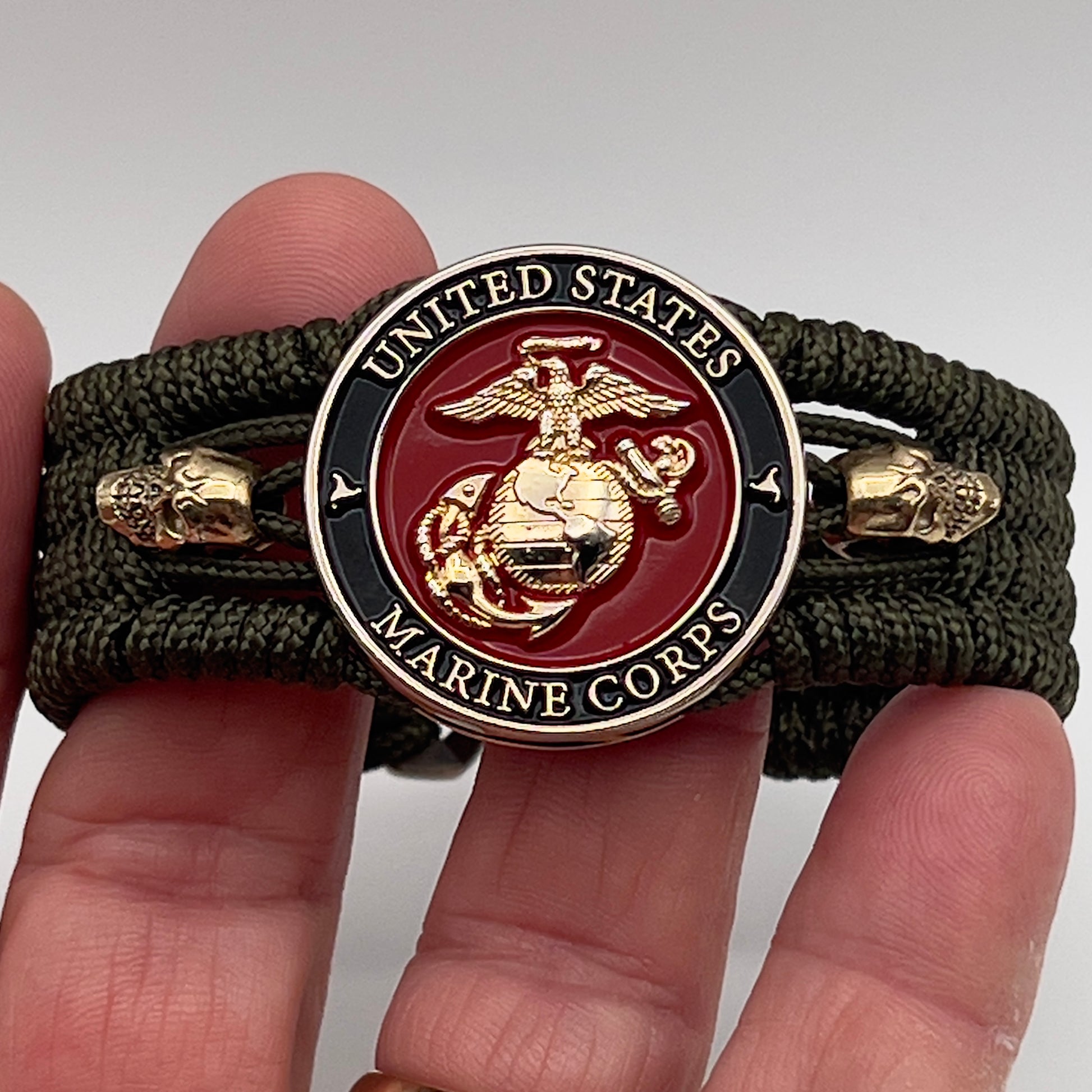 Thin, medium width, flexible and comfortable braided United States Marine Corps bracelet featuring a 24K gold plated USMC officer Eagle Globe and Anchor medallion, two gold plated skulls, a gold Cobra style tactical buckle and woven with Olive Drab Type-1 paracord.