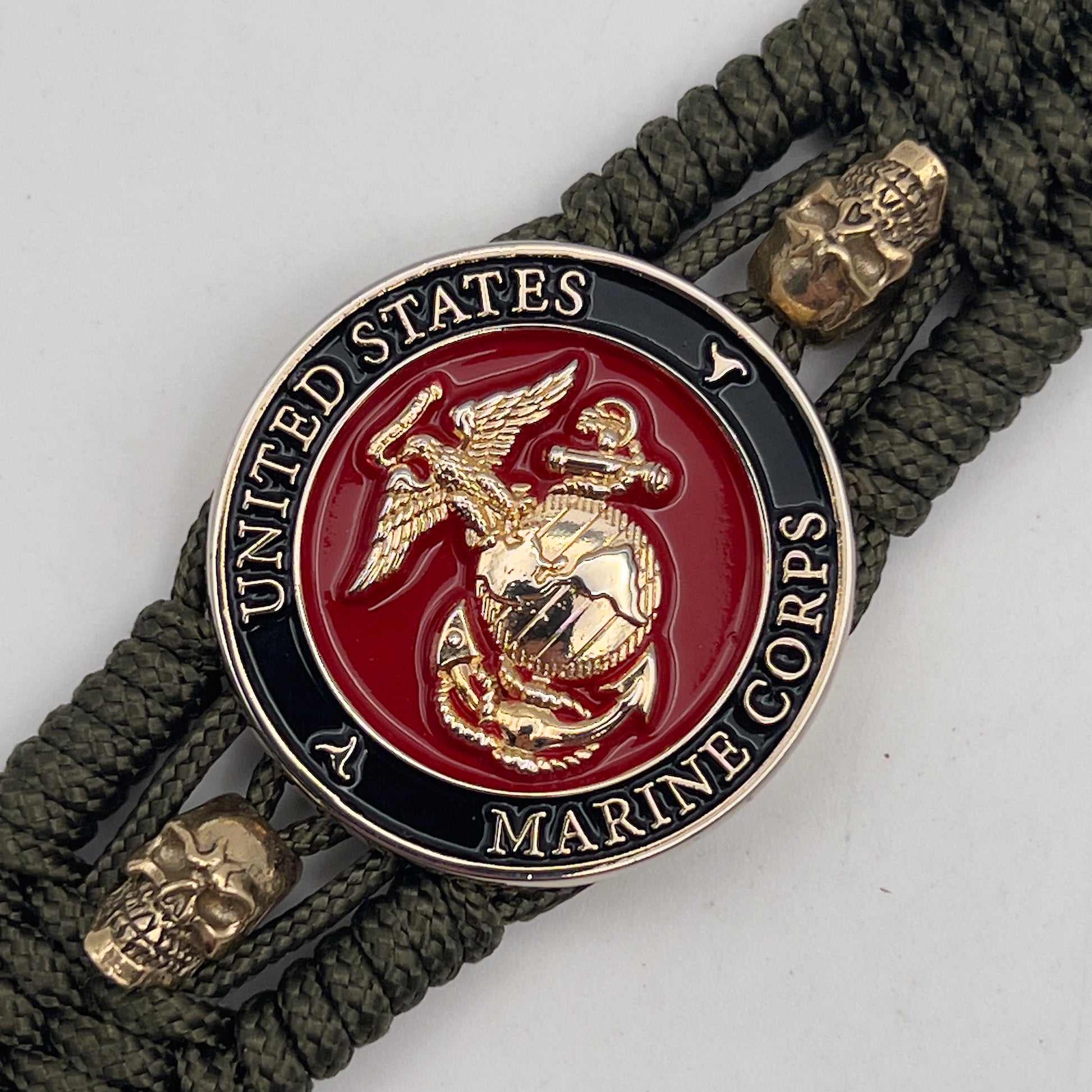 Thin, medium width, flexible and comfortable braided United States Marine Corps bracelet featuring a 24K gold plated USMC officer Eagle Globe and Anchor medallion, two gold plated skulls, a gold Cobra style tactical buckle and woven with Olive Drab Type-1 paracord.