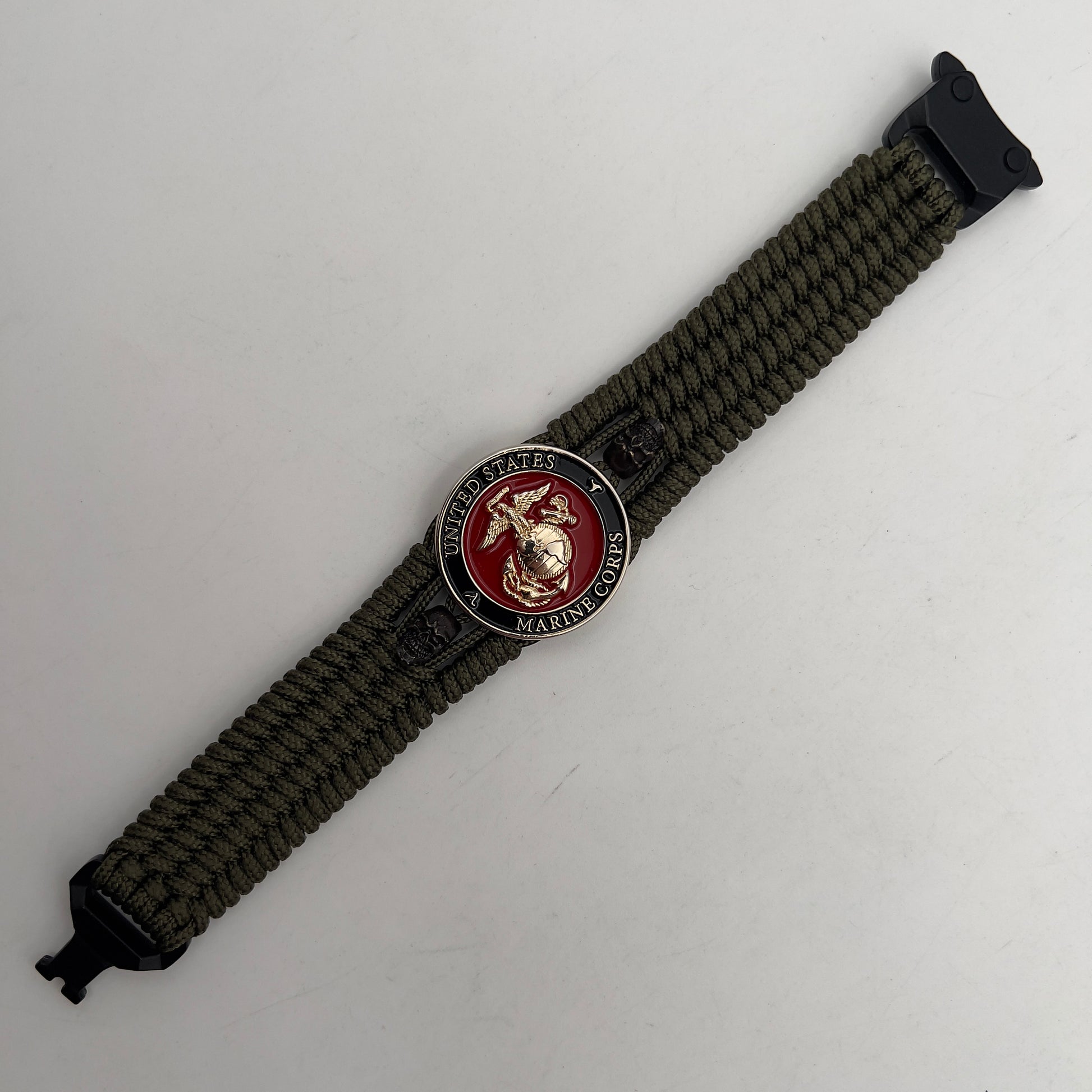 Thin, medium width, flexible and comfortable braided United States Marine Corps bracelet featuring a 24K gold plated USMC officer Eagle Globe and Anchor medallion, two black micro skulls, a black Cobra style tactical buckle and woven with Olive Drab Type-1 paracord.