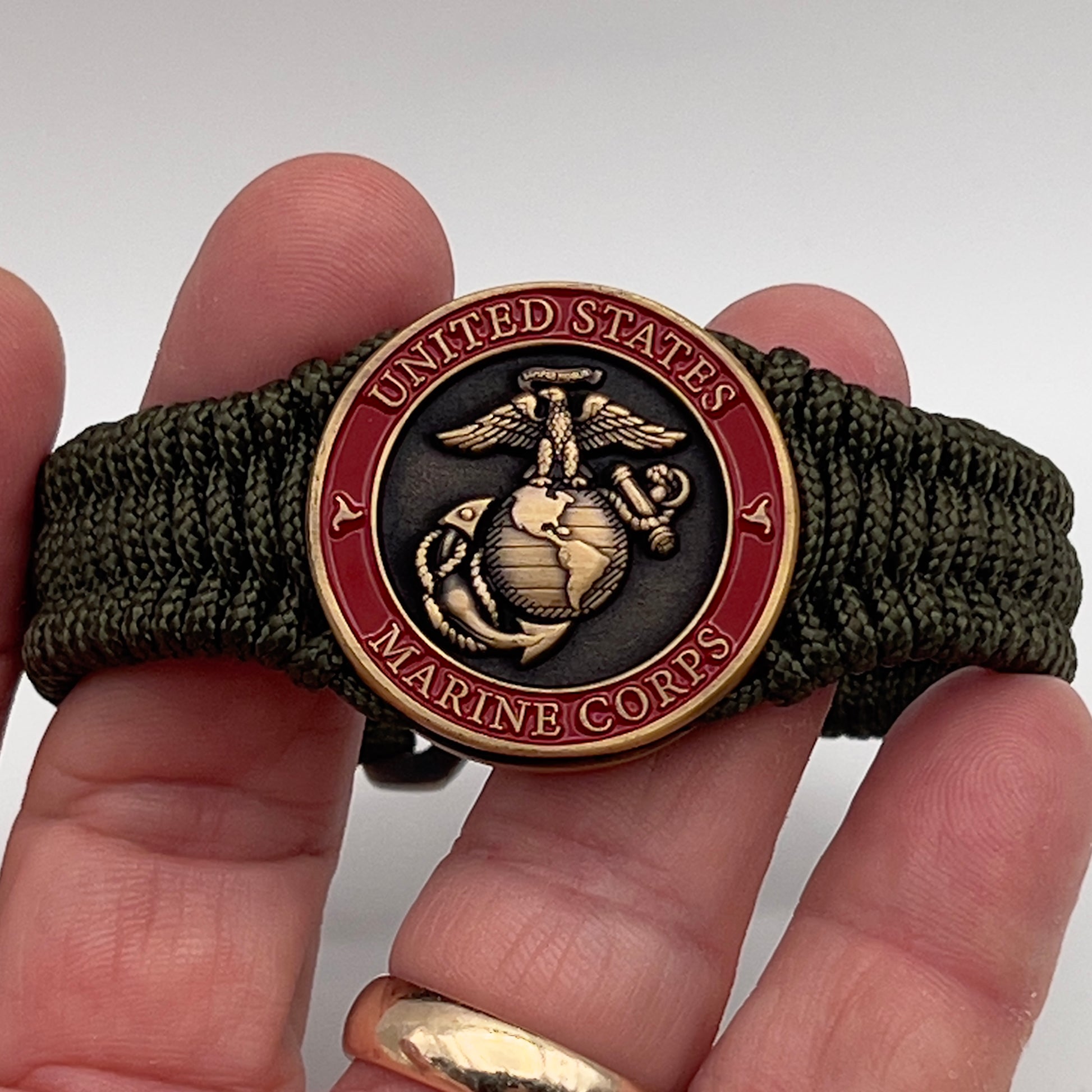 Thin, narrow, flexible and comfortable braided United States Marine Corps bracelet featuring a 24K antique gold plated USMC Eagle Globe and Anchor medallion, a gold Cobra style tactical buckle and woven with Olive Drab Type-1 paracord.
