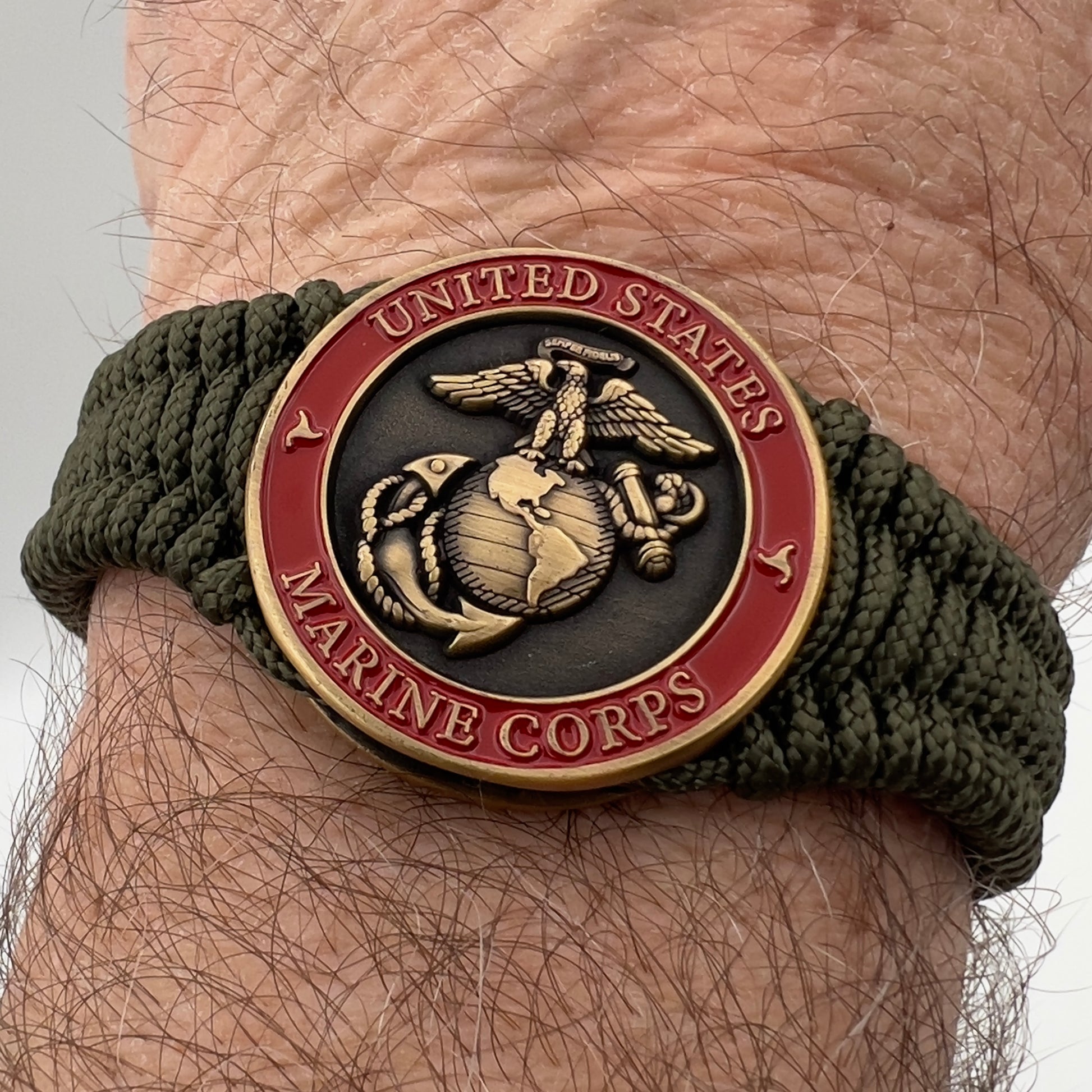 Thin, narrow, flexible and comfortable braided United States Marine Corps bracelet featuring a 24K antique gold plated USMC Eagle Globe and Anchor medallion, a gold Cobra style tactical buckle and woven with Olive Drab Type-1 paracord.