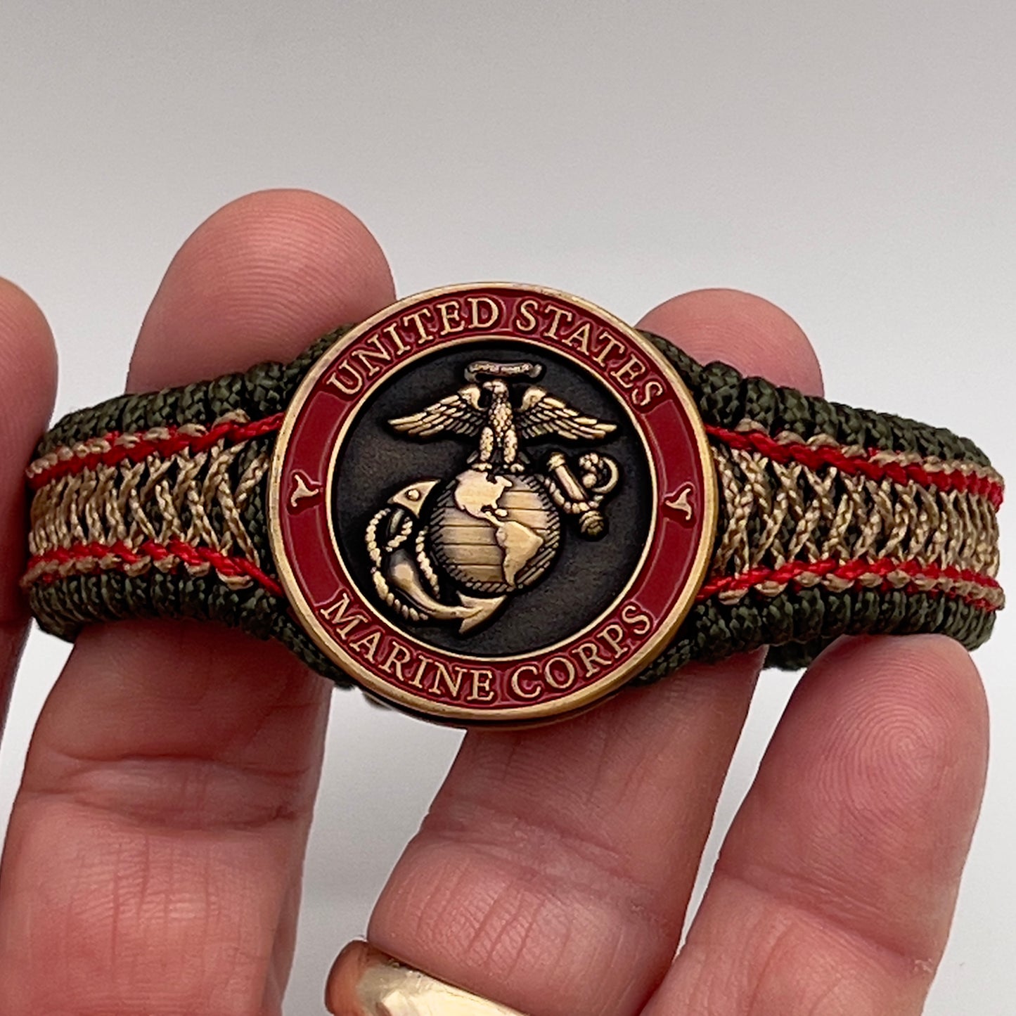 Thin, narrow, flexible and comfortable braided United States Marine Corps bracelet featuring a 24K antique gold plated USMC Eagle Globe and Anchor medallion, a gold Cobra style tactical buckle and woven with Olive Drab Type-1 paracord and Imperial Red and Gold nano cord.