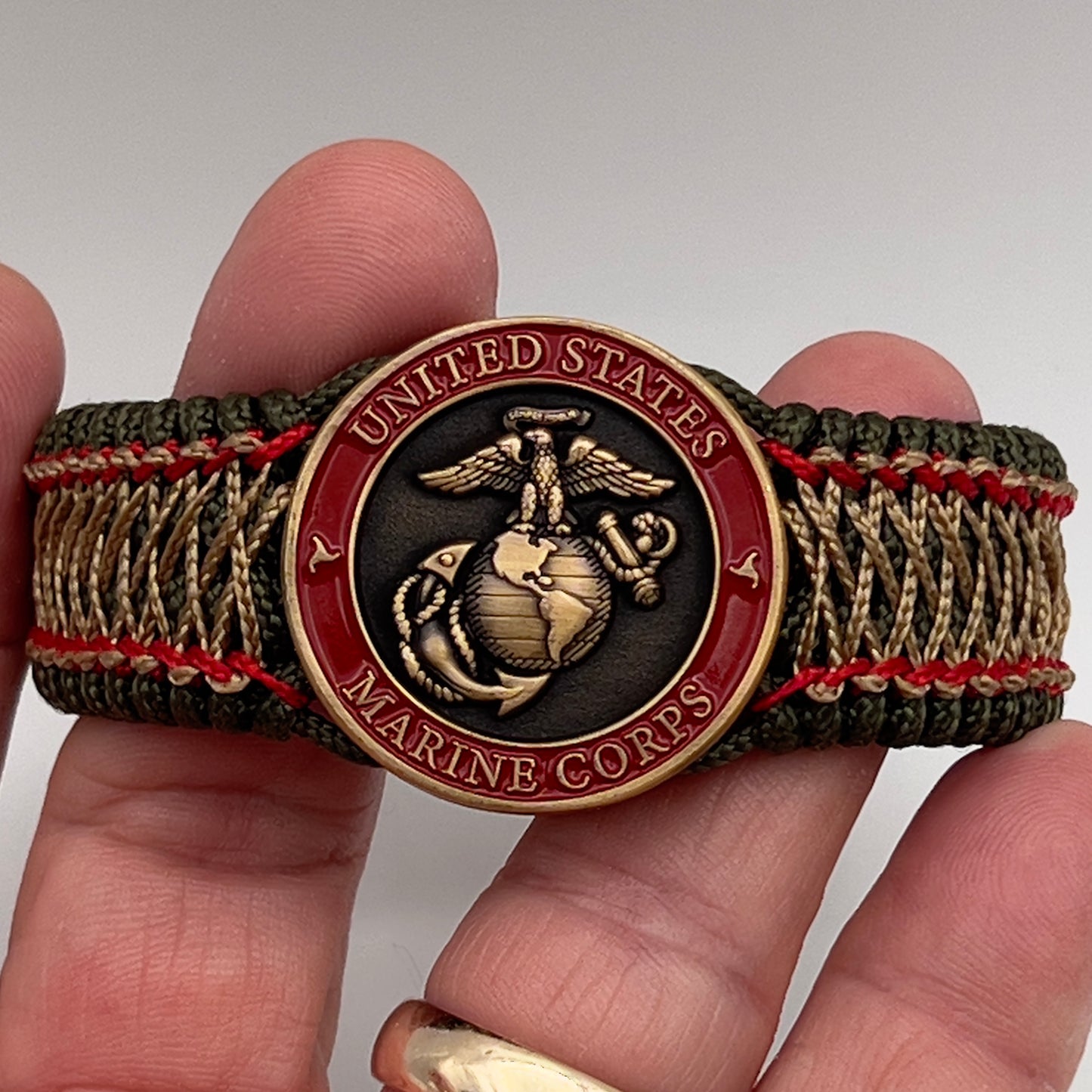 Thin, medium width, flexible and comfortable braided United States Marine Corps bracelet featuring a 24K antique gold plated USMC Eagle Globe and Anchor medallion, a gold Cobra style tactical buckle and woven with Olive Drab Type-1 paracord and Imperial Red and Gold nano cord.