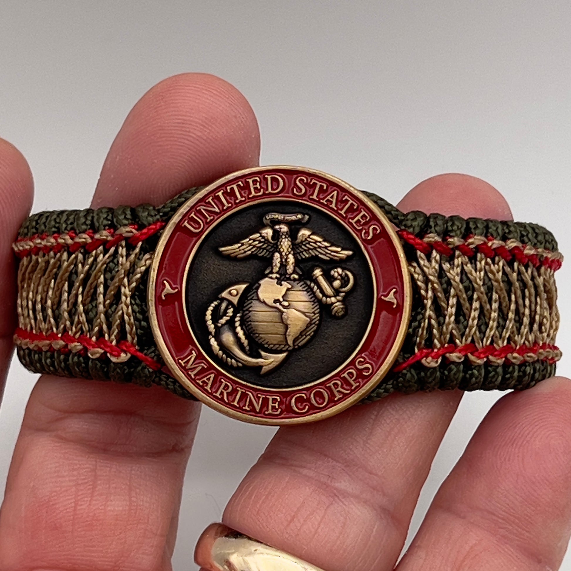 Thin, medium width, flexible and comfortable braided United States Marine Corps bracelet featuring a 24K antique gold plated USMC Eagle Globe and Anchor medallion, a gold Cobra style tactical buckle and woven with Olive Drab Type-1 paracord and Imperial Red and Gold nano cord.