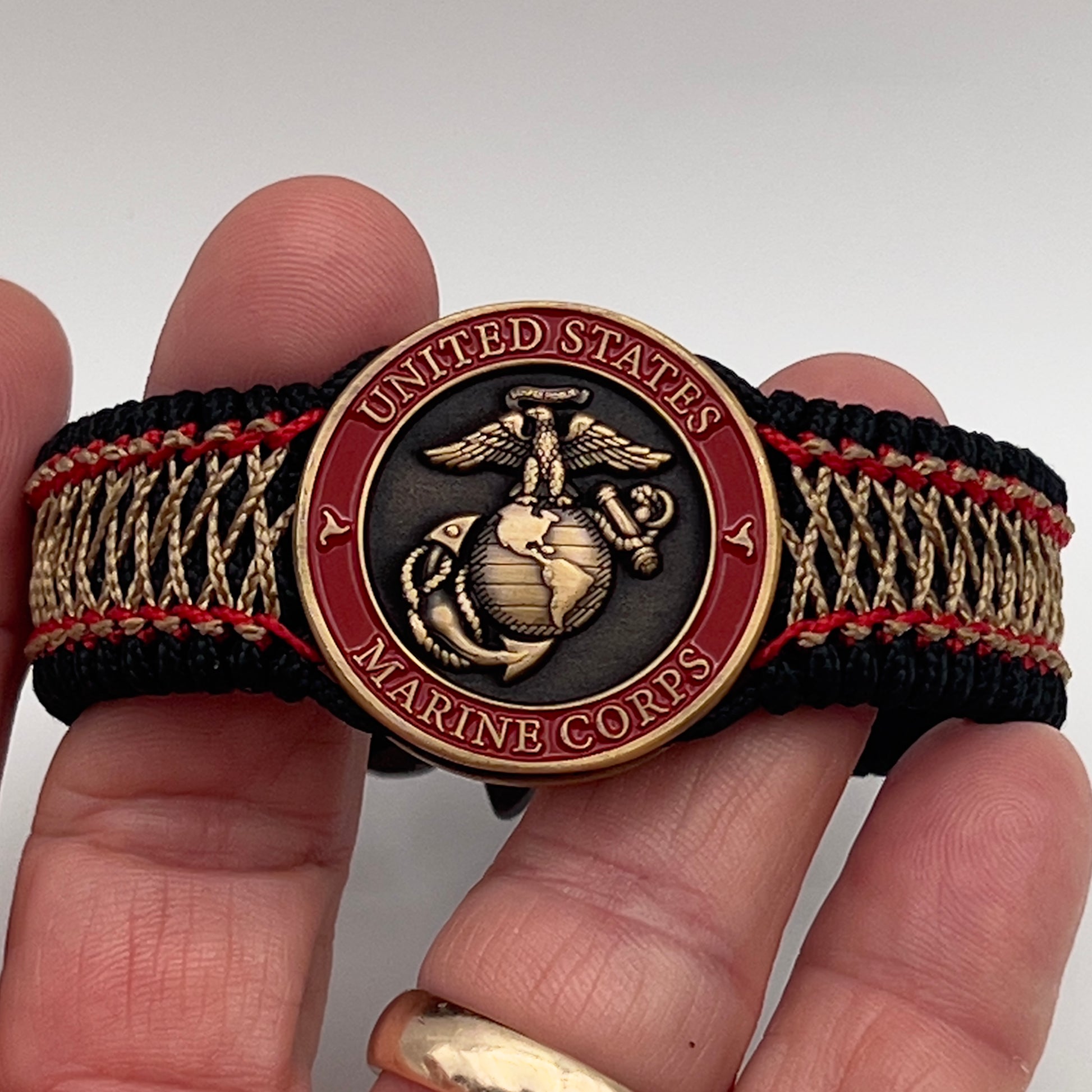 Thin, medium width, flexible and comfortable braided United States Marine Corps bracelet featuring a 24K antique gold plated USMC Eagle Globe and Anchor medallion, a black Cobra style tactical buckle and woven with black Type-1 paracord and Imperial Red and Gold nano cord.