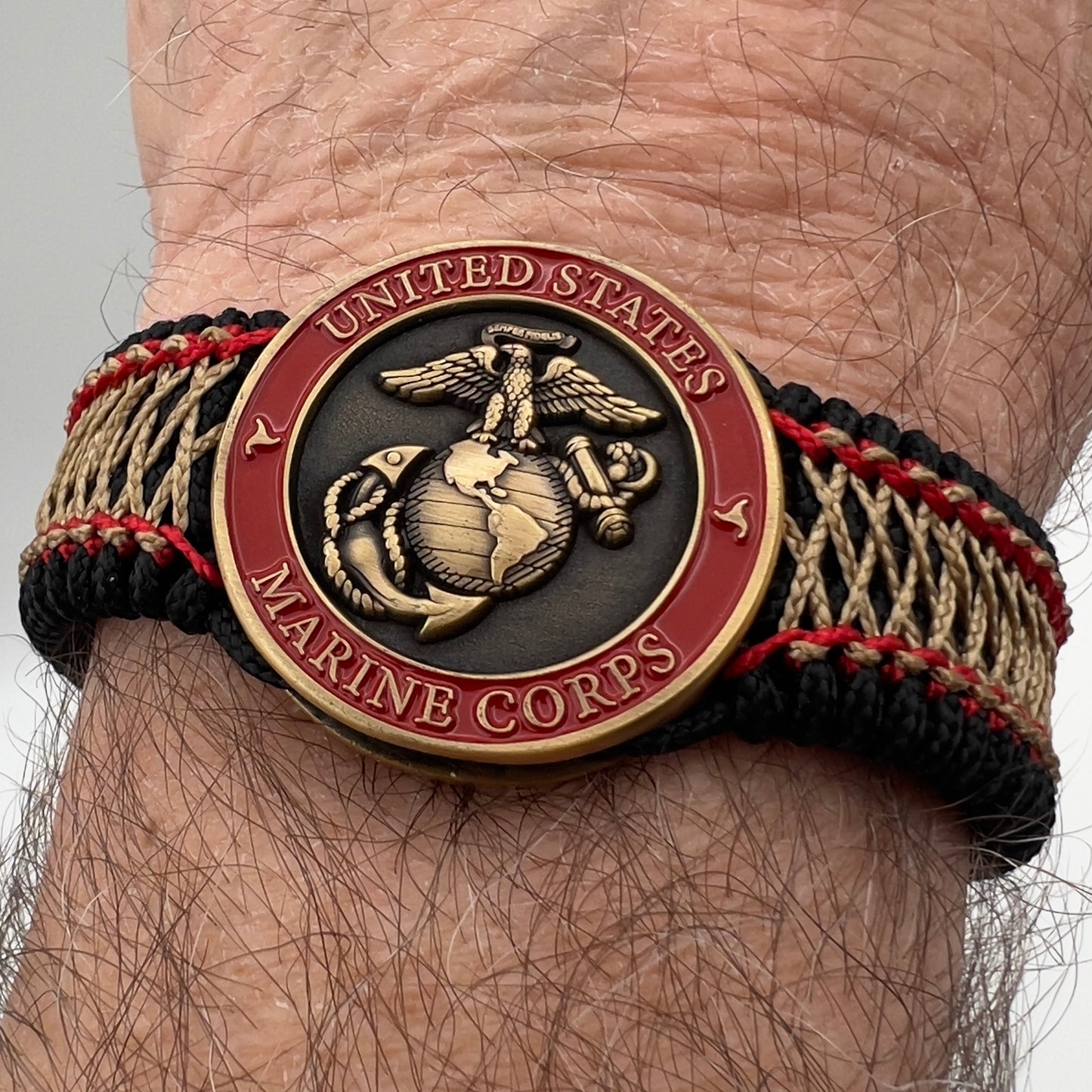 Thin, medium width, flexible and comfortable braided United States Marine Corps bracelet featuring a 24K antique gold plated USMC Eagle Globe and Anchor medallion, a black Cobra style tactical buckle and woven with black Type-1 paracord and Imperial Red and Gold nano cord.
