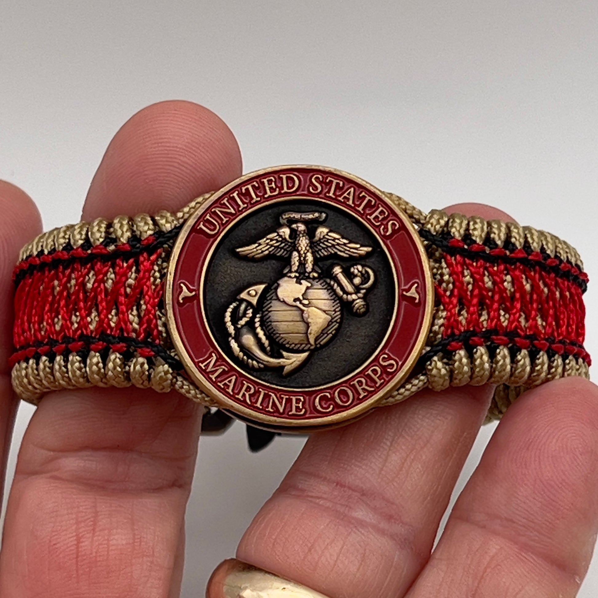 Thin, medium width, flexible and comfortable braided United States Marine Corps bracelet featuring a 24K antique gold plated USMC Eagle Globe and Anchor medallion, a gold Cobra style tactical buckle and woven with gold Type-1 paracord and Imperial Red and Black nano cord.