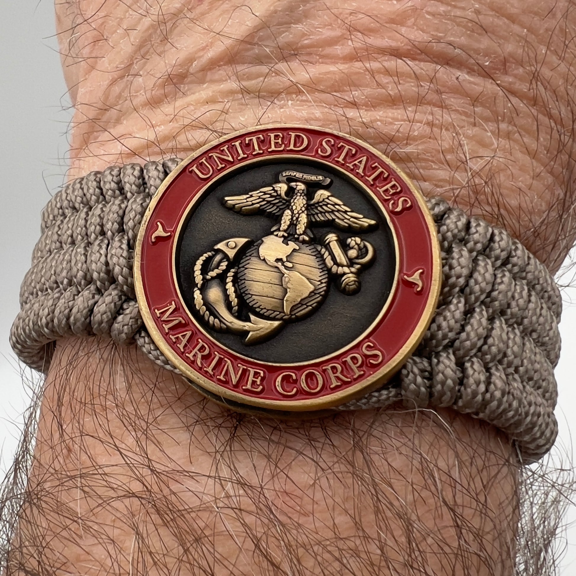 Thin, medium wide, flexible and comfortable braided United States Marine Corps bracelet featuring a 24K antique gold plated USMC Eagle Globe and Anchor medallion, a gold Cobra style tactical buckle and woven with Tan Type-1 paracord.