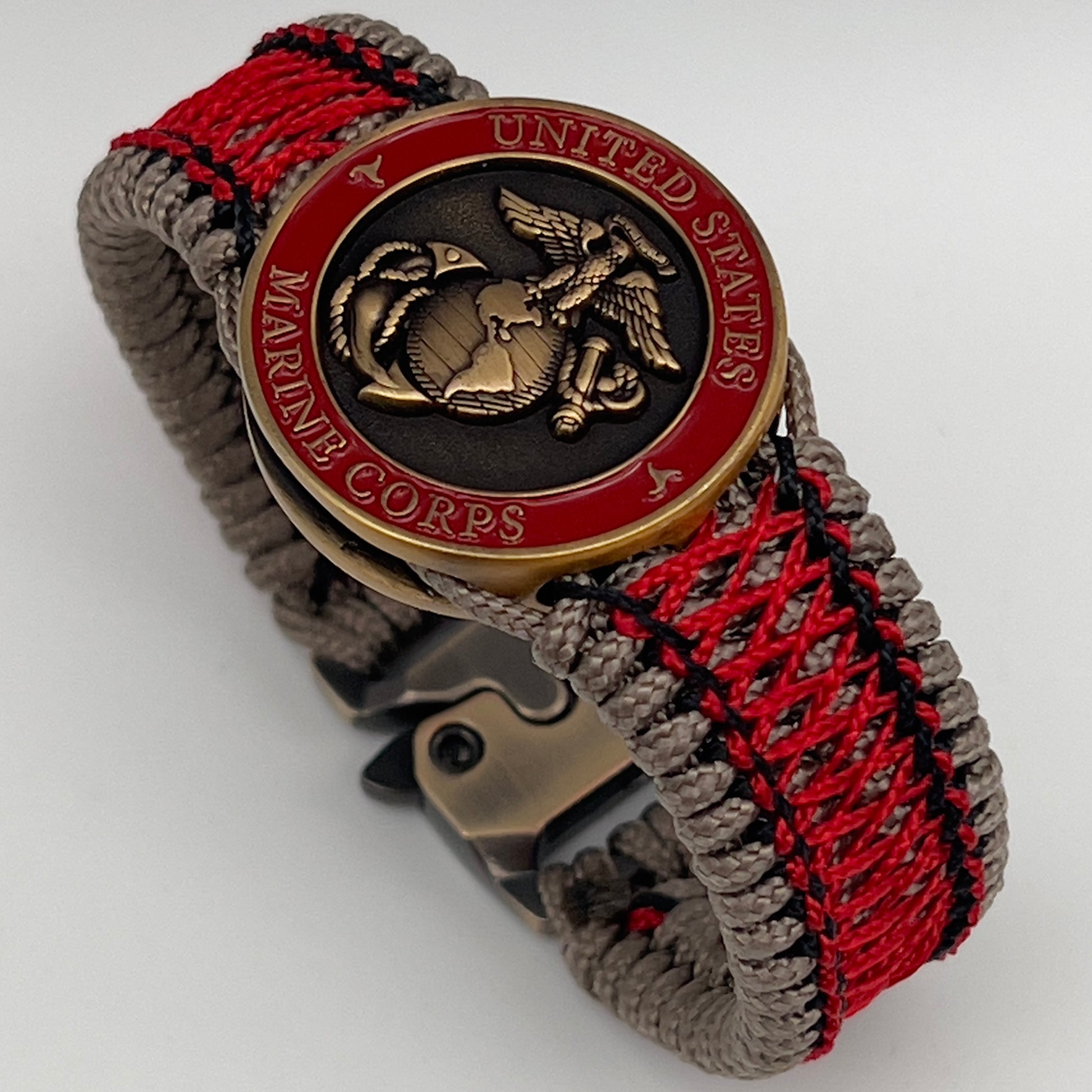 Thin, medium width, flexible and comfortable braided United States Marine Corps bracelet featuring a 24K antique gold plated USMC Eagle Globe and Anchor medallion, a gold Cobra style tactical buckle and woven with Tan Type-1 paracord and Imperial Red and Black nano cord.