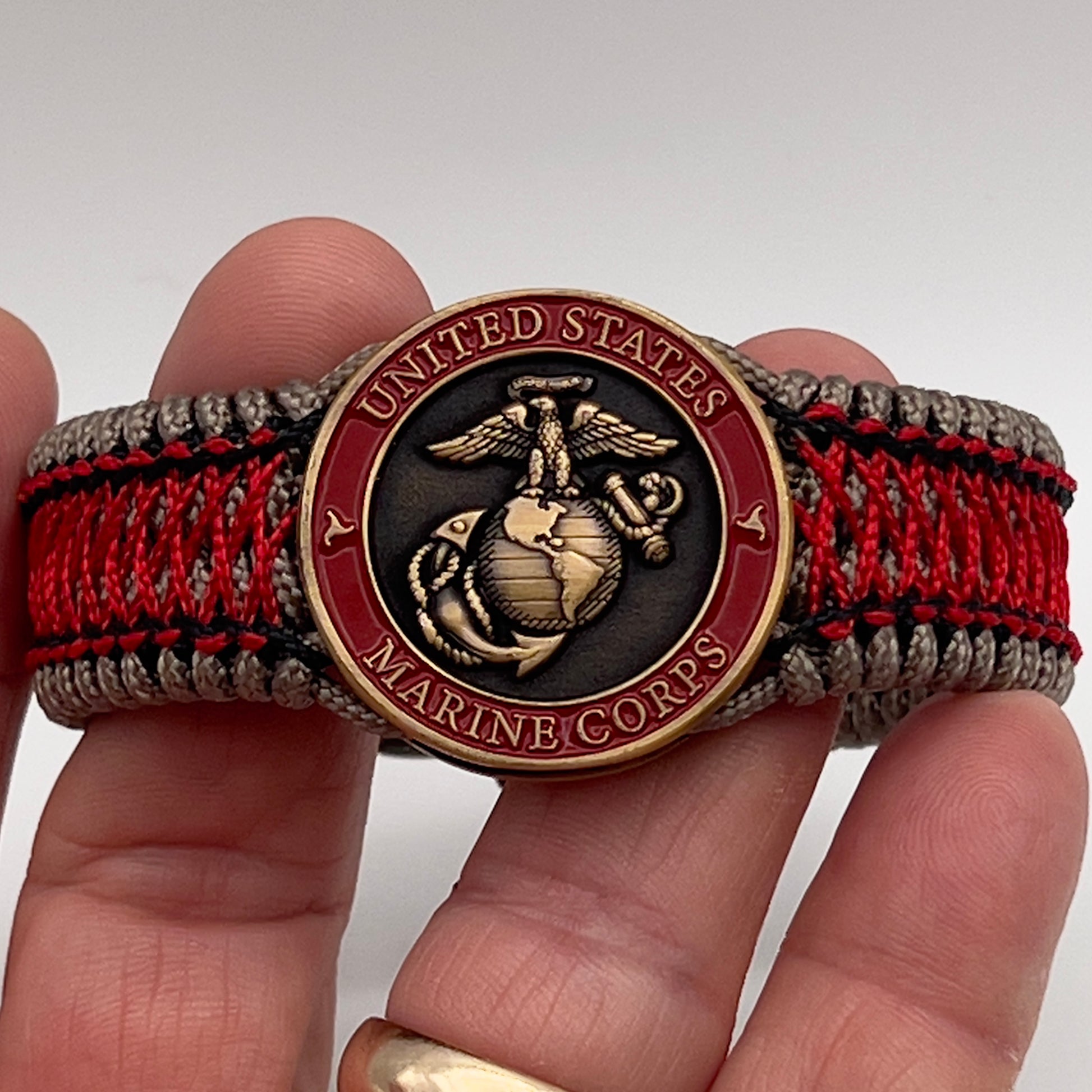 Thin, medium width, flexible and comfortable braided United States Marine Corps bracelet featuring a 24K antique gold plated USMC Eagle Globe and Anchor medallion, a gold Cobra style tactical buckle and woven with Tan Type-1 paracord and Imperial Red and Black nano cord.