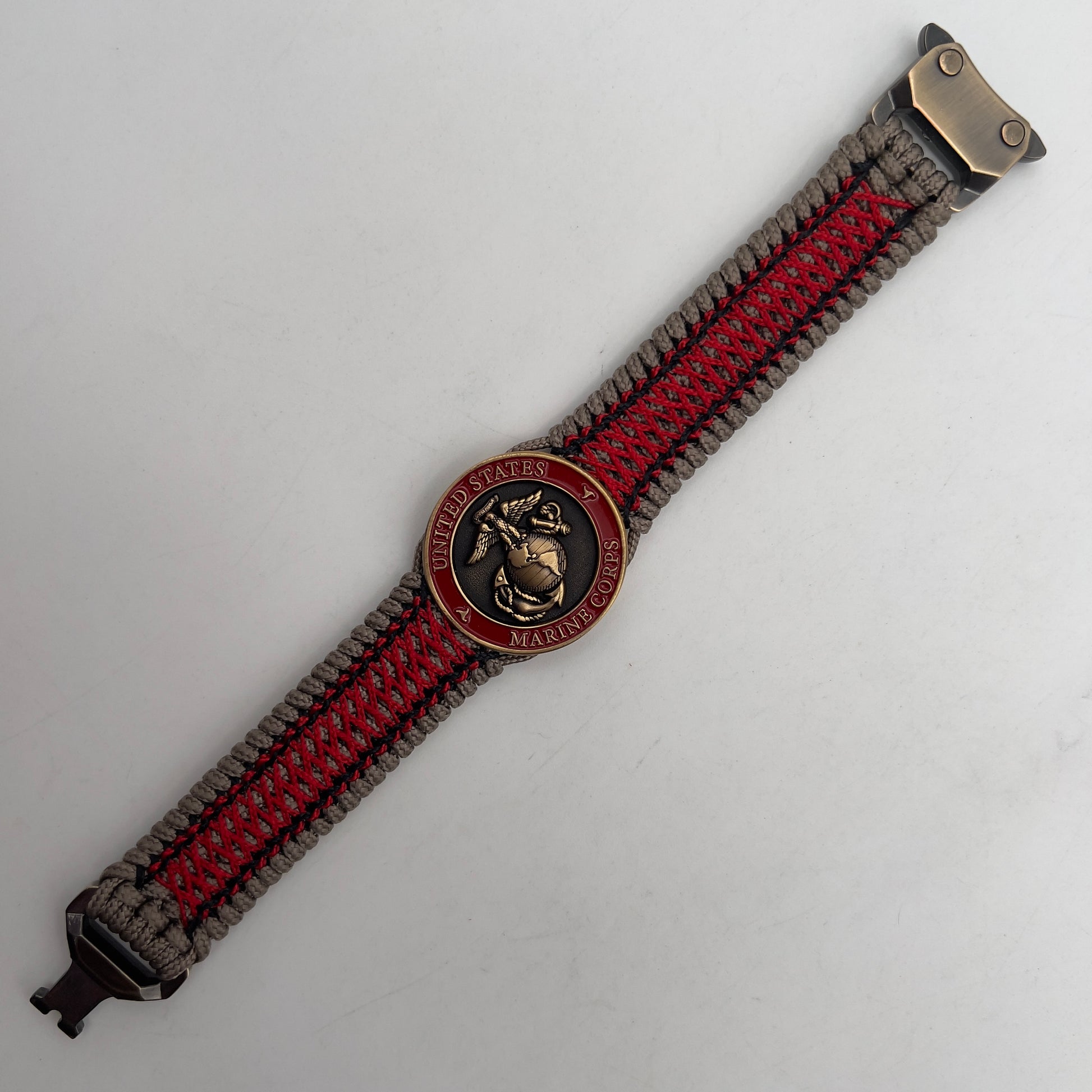 Thin, medium width, flexible and comfortable braided United States Marine Corps bracelet featuring a 24K antique gold plated USMC Eagle Globe and Anchor medallion, a gold Cobra style tactical buckle and woven with Tan Type-1 paracord and Imperial Red and Black nano cord.
