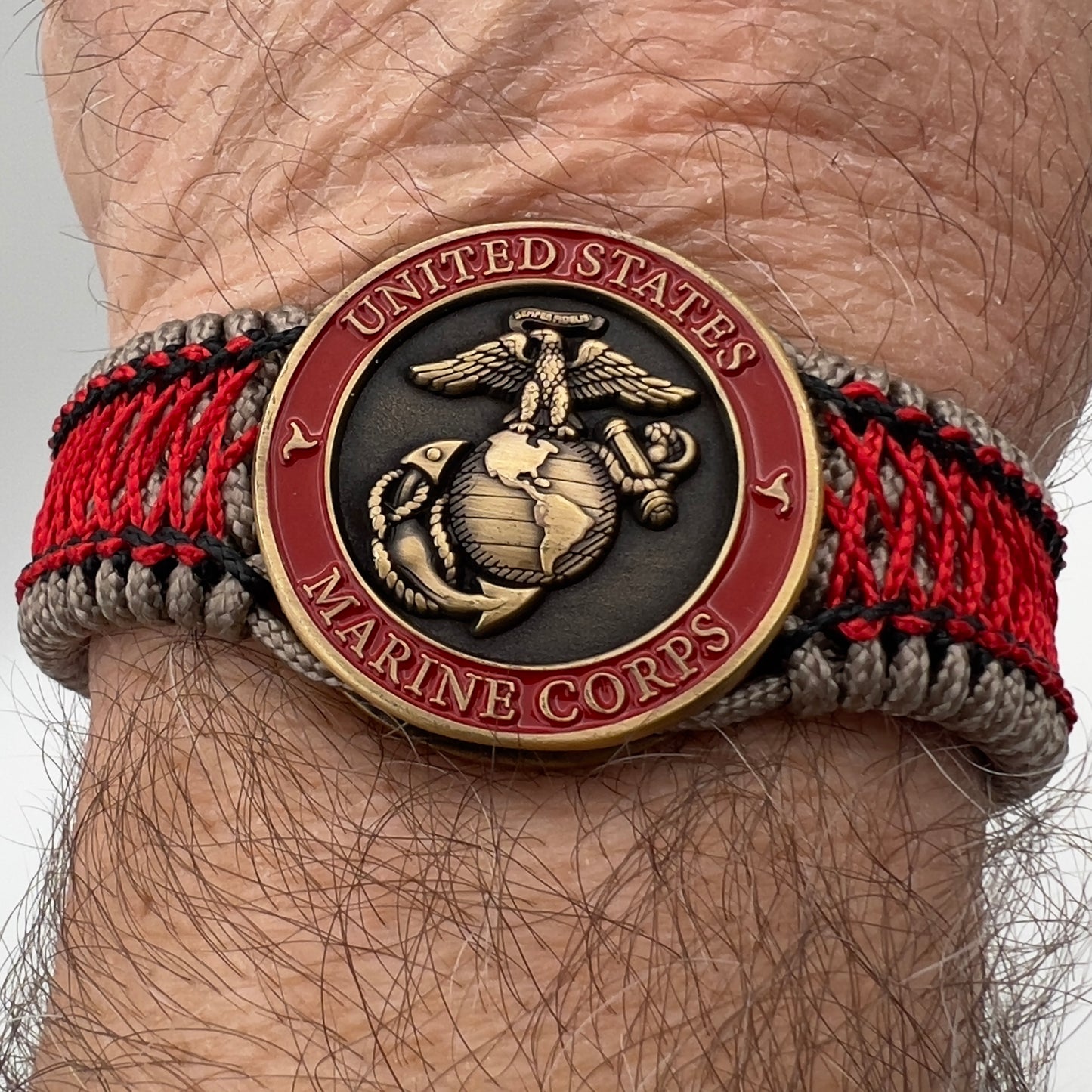 Thin, medium width, flexible and comfortable braided United States Marine Corps bracelet featuring a 24K antique gold plated USMC Eagle Globe and Anchor medallion, a gold Cobra style tactical buckle and woven with Tan Type-1 paracord and Imperial Red and Black nano cord.