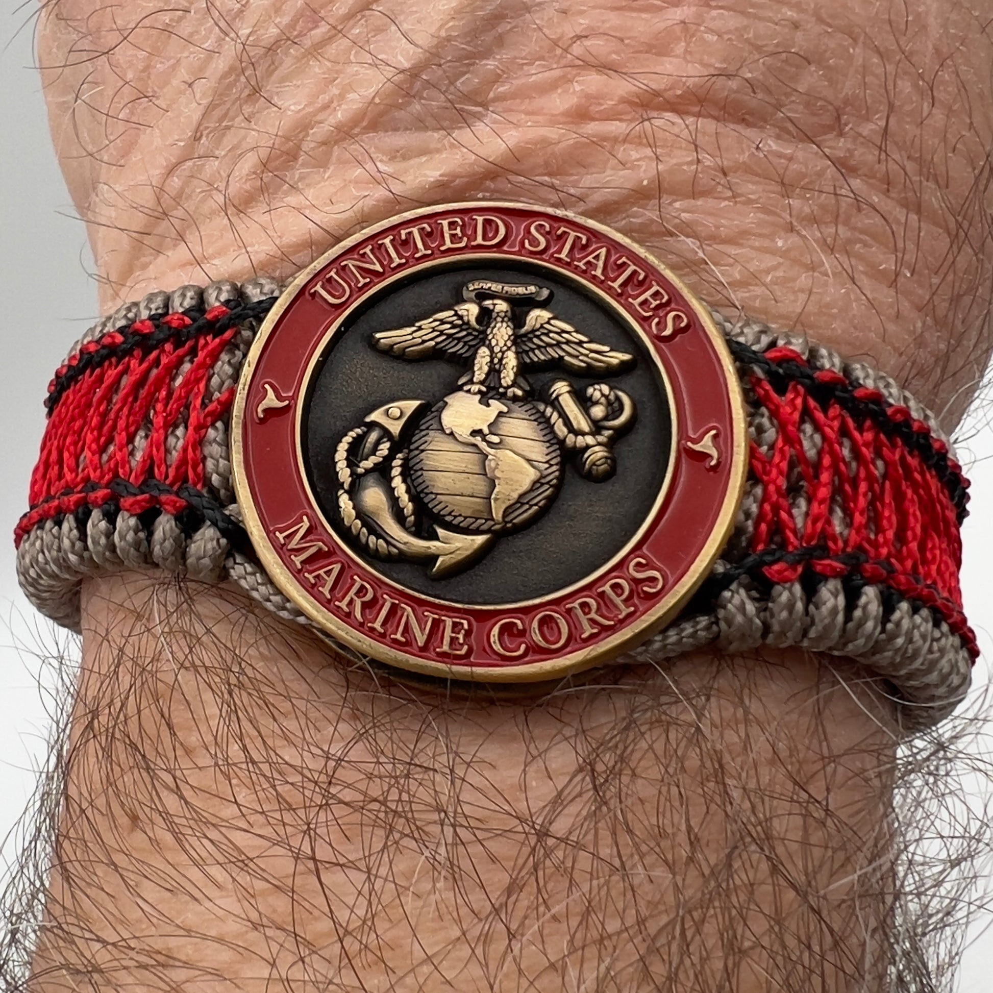Thin, medium width, flexible and comfortable braided United States Marine Corps bracelet featuring a 24K antique gold plated USMC Eagle Globe and Anchor medallion, a gold Cobra style tactical buckle and woven with Tan Type-1 paracord and Imperial Red and Black nano cord.