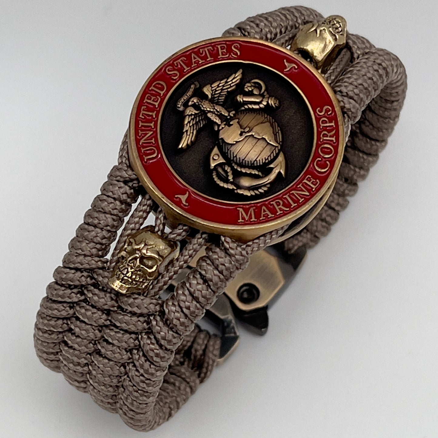 Thin, medium width, flexible and comfortable braided United States Marine Corps bracelet featuring a 24K antique gold plated USMC officer Eagle Globe and Anchor medallion, two gold plated skulls, a gold Cobra style tactical buckle and woven with tan Type-1 paracord.