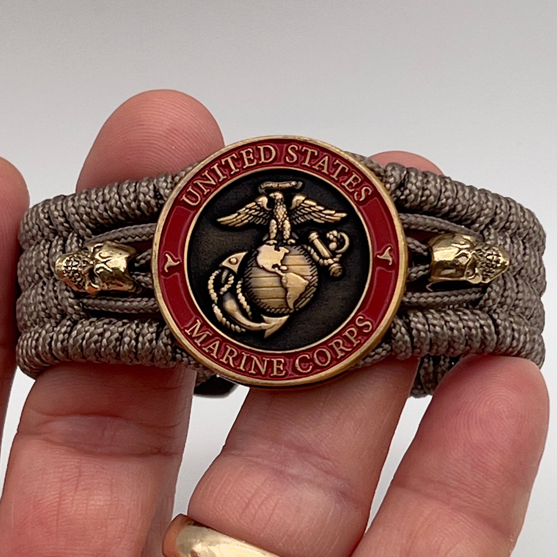 Thin, medium width, flexible and comfortable braided United States Marine Corps bracelet featuring a 24K antique gold plated USMC officer Eagle Globe and Anchor medallion, two gold plated skulls, a gold Cobra style tactical buckle and woven with tan Type-1 paracord.