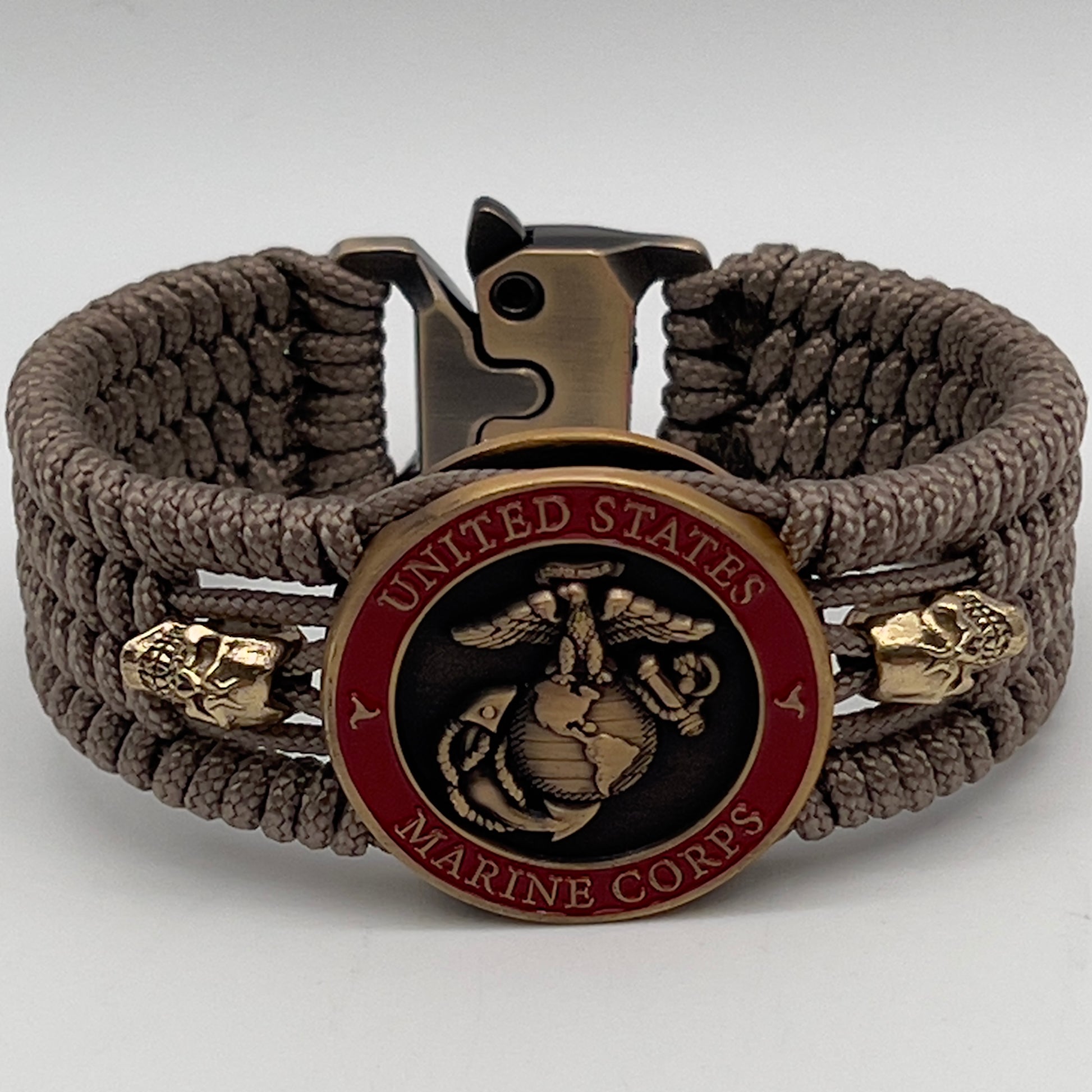 Thin, medium width, flexible and comfortable braided United States Marine Corps bracelet featuring a 24K antique gold plated USMC officer Eagle Globe and Anchor medallion, two gold plated skulls, a gold Cobra style tactical buckle and woven with tan Type-1 paracord.