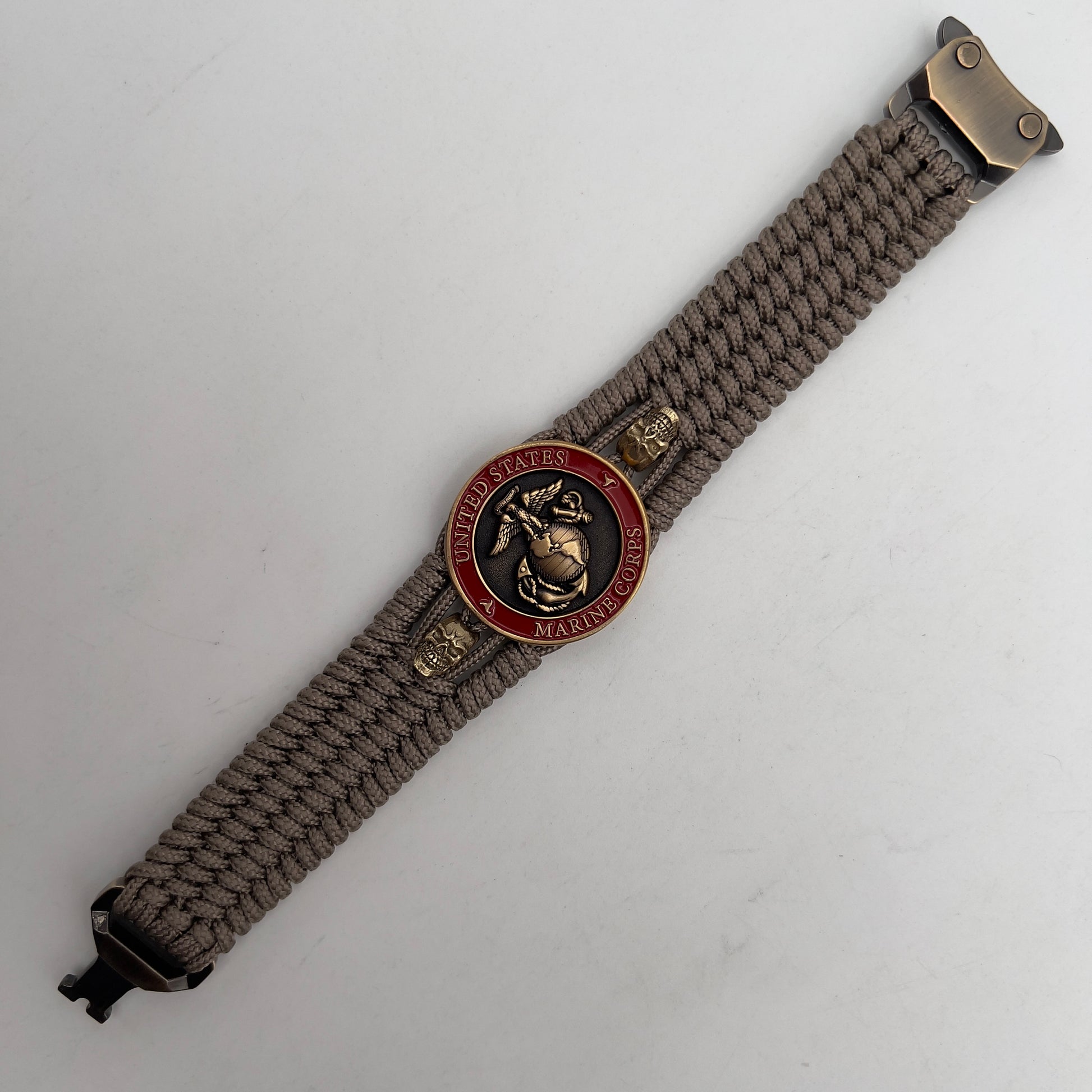Thin, medium width, flexible and comfortable braided United States Marine Corps bracelet featuring a 24K antique gold plated USMC officer Eagle Globe and Anchor medallion, two gold plated skulls, a gold Cobra style tactical buckle and woven with tan Type-1 paracord.