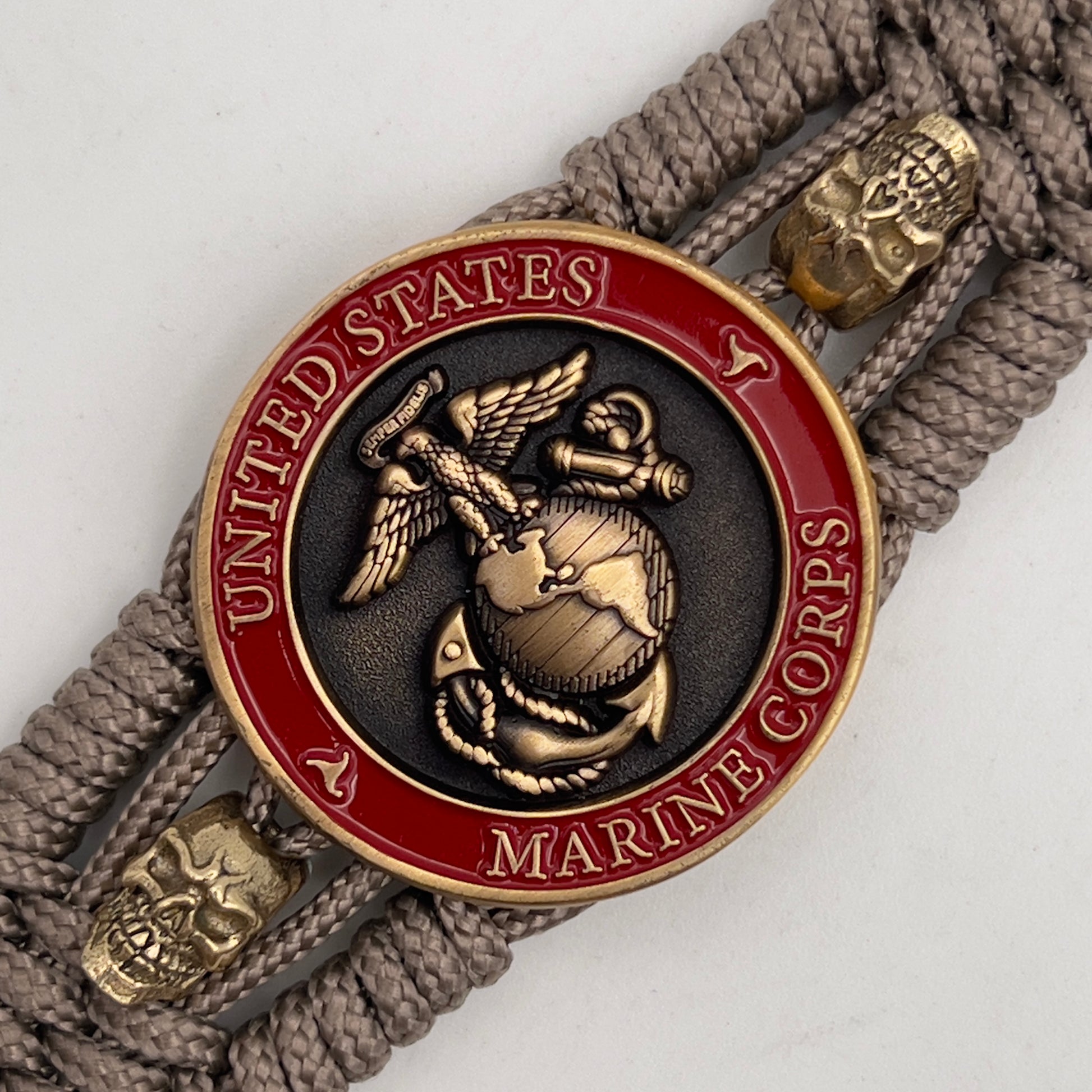 Thin, medium width, flexible and comfortable braided United States Marine Corps bracelet featuring a 24K antique gold plated USMC officer Eagle Globe and Anchor medallion, two gold plated skulls, a gold Cobra style tactical buckle and woven with tan Type-1 paracord.